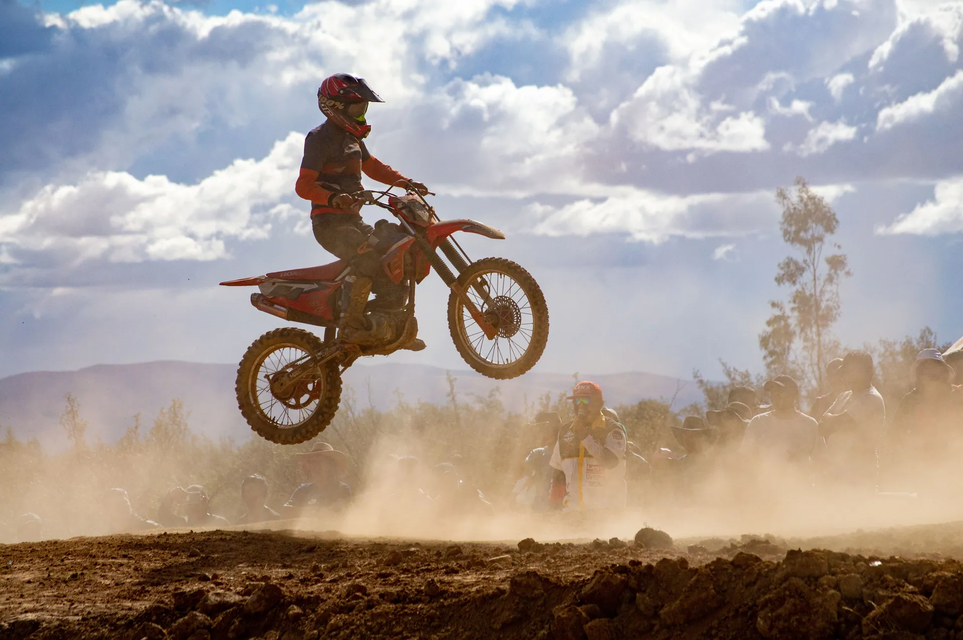 A thrilling scene of a biker catching air during an off-road motorcycle race, surrounded by a dusty landscape and spectators.