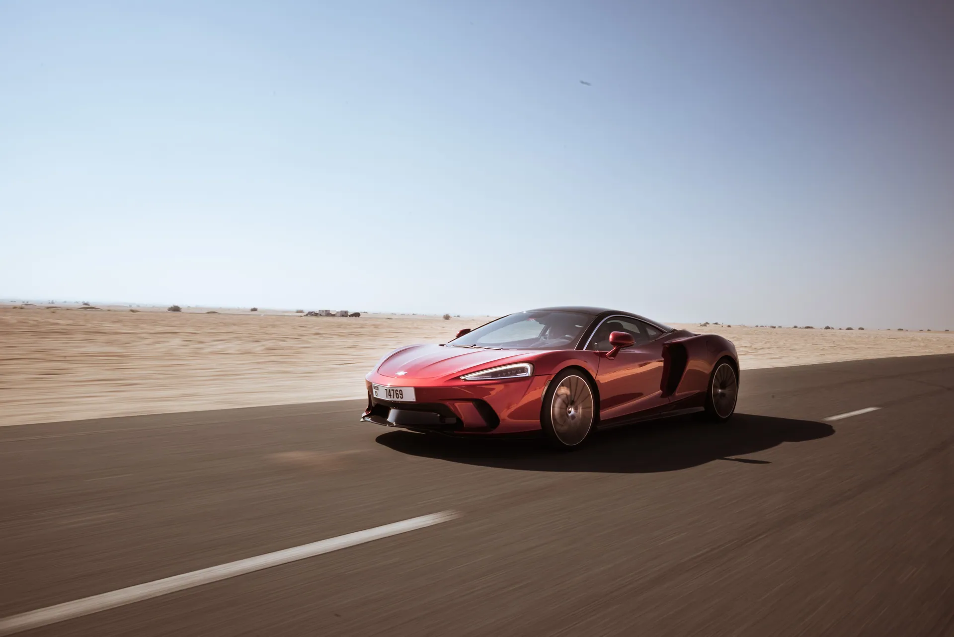 A sleek red sports car racing along a deserted highway under a clear blue sky.