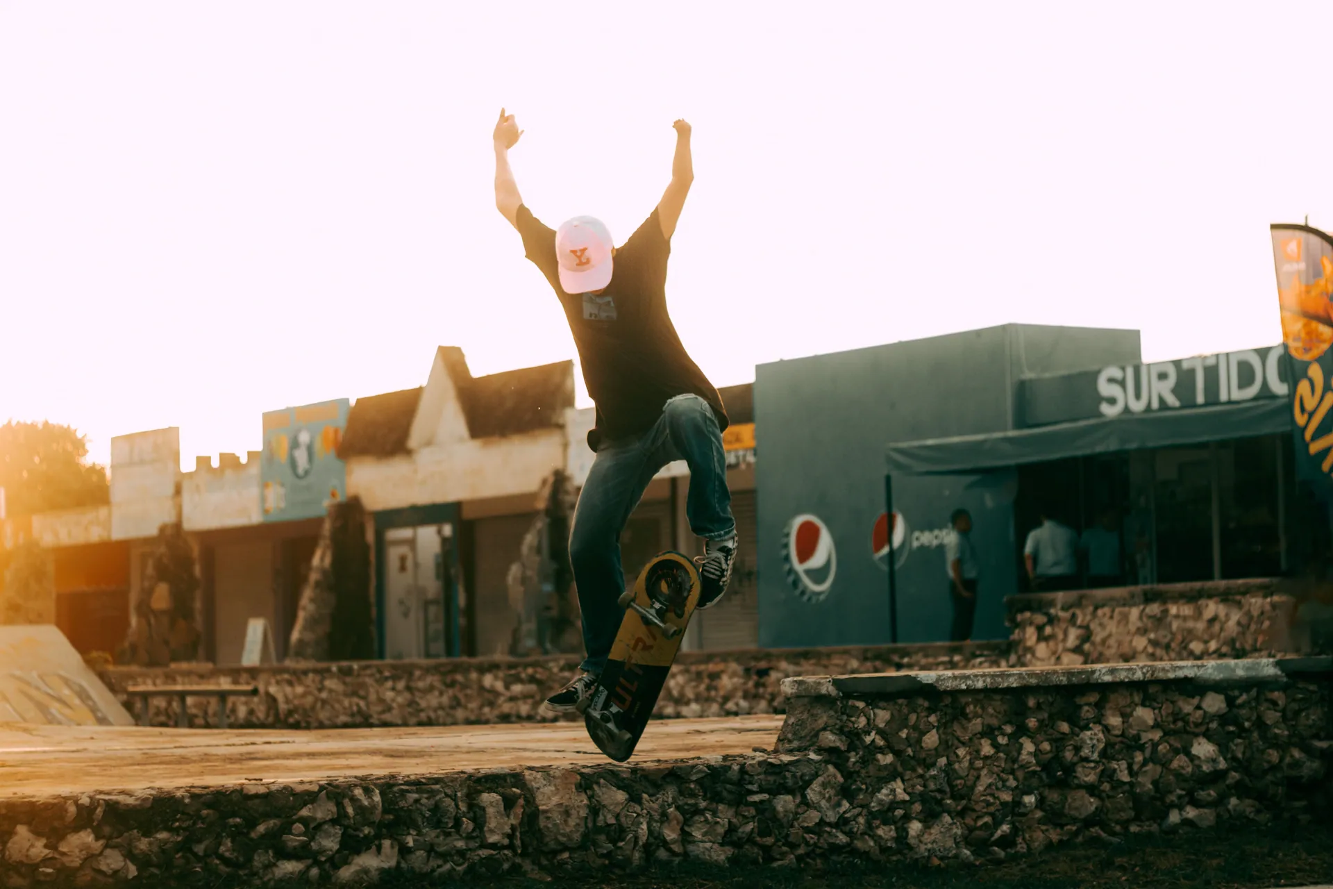 A skateboarder in midair executing a trick during sunset at an outdoor skatepark.