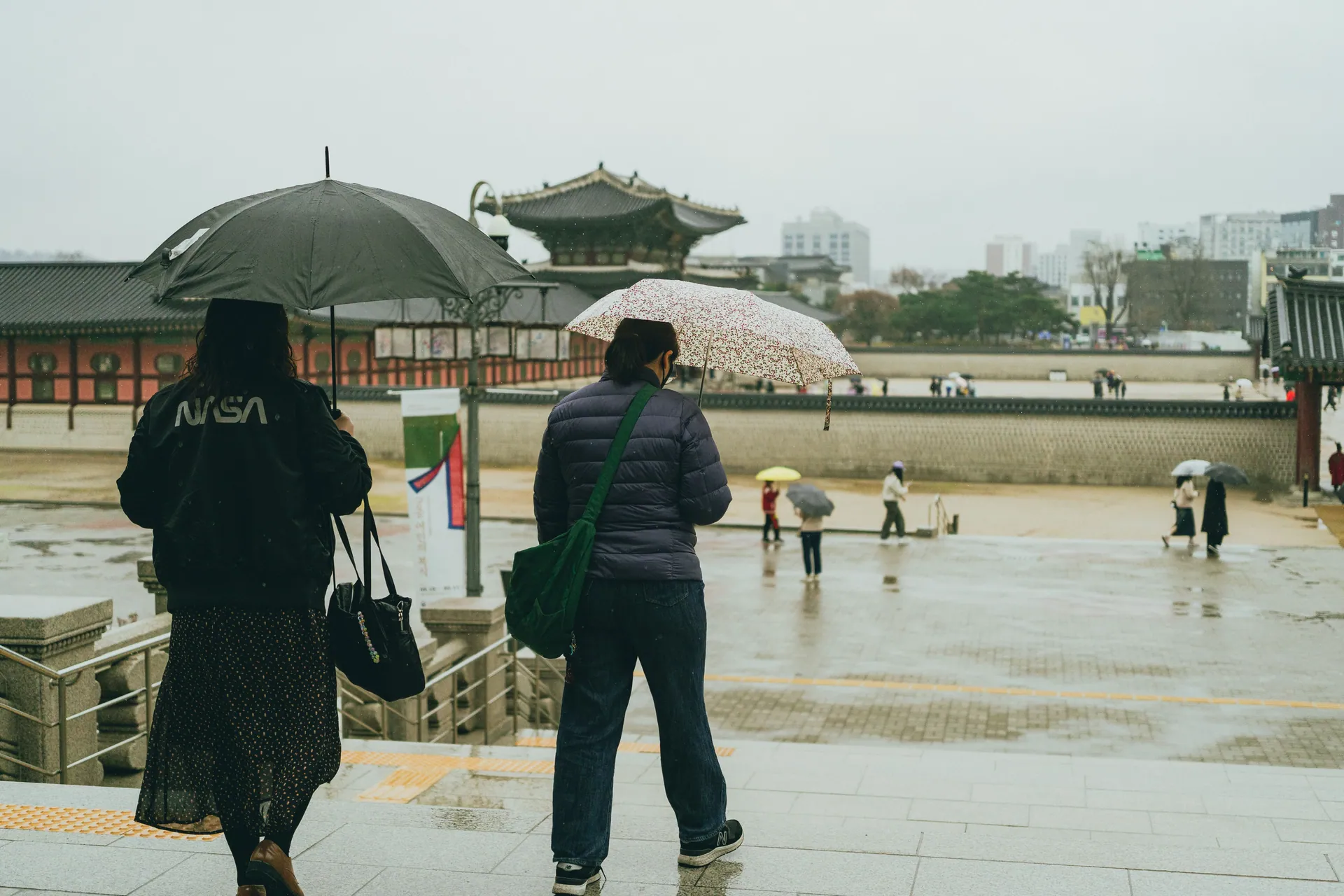 Visitors with umbrellas explore Gyeongbokgung Palace on a rainy day in Seoul, South Korea.