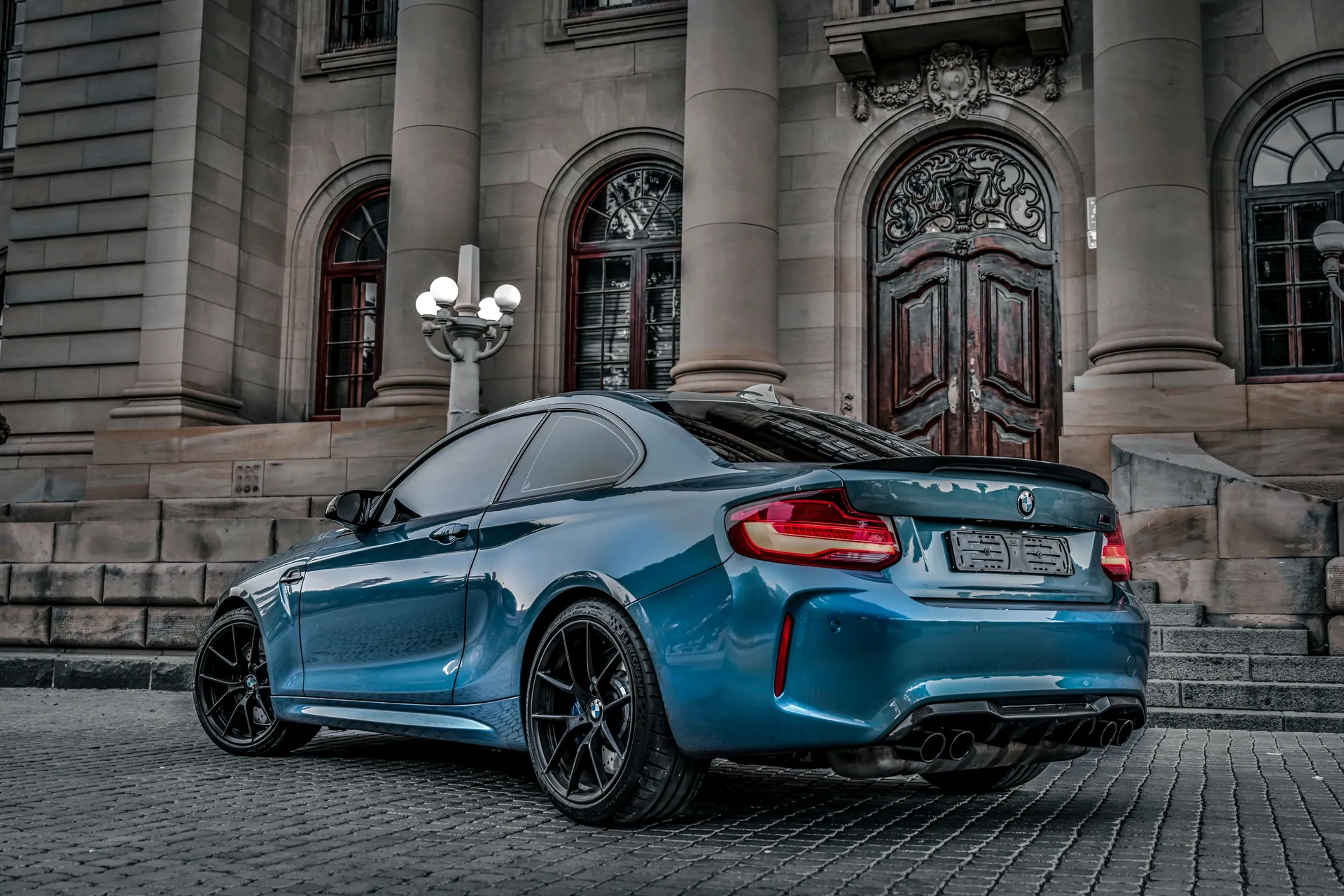 A sleek blue luxury car parked outside a grand historic building, showcasing elegance and style.