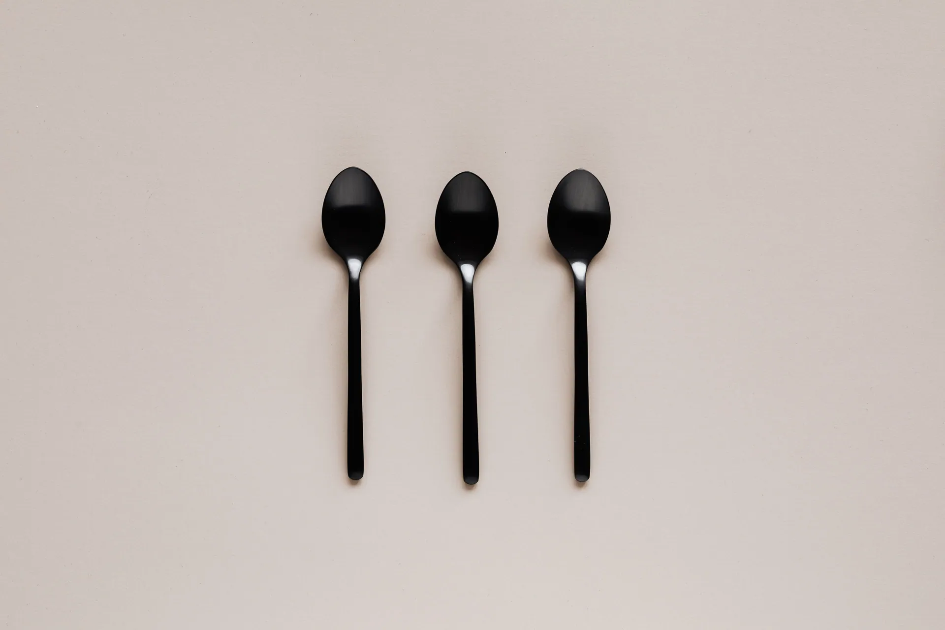 Top view of black teaspoon placed in line on beige background