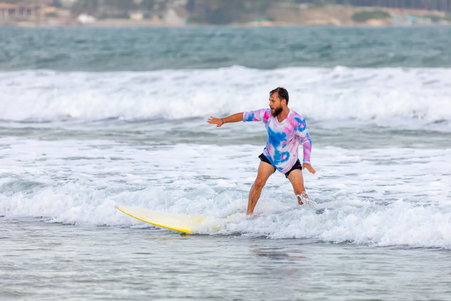 A man in a colorful shirt rides a yellow surfboard in ocean waves, showing balance and fun.