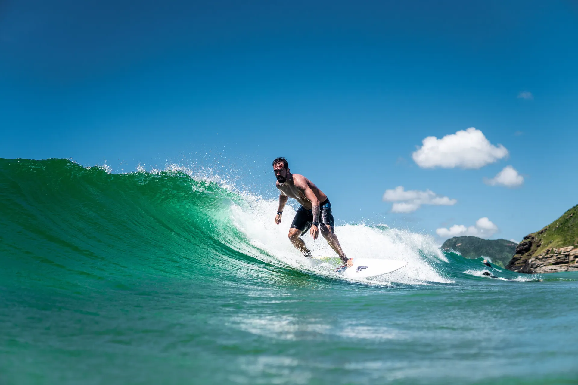 A surfer skillfully rides a vibrant green wave under a clear blue sky.