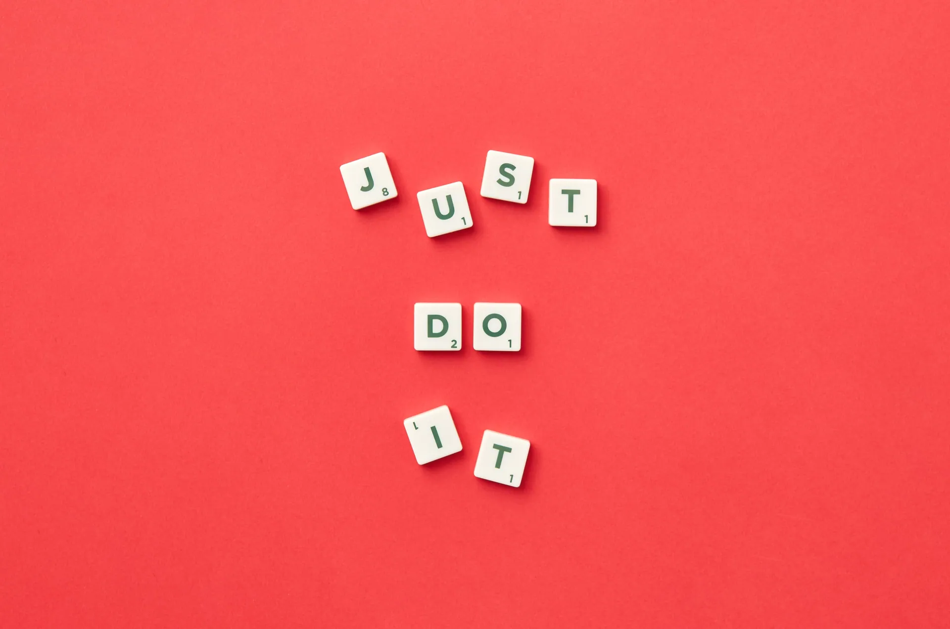 Motivational phrase 'Just Do It' spelled with Scrabble letters on a red background.