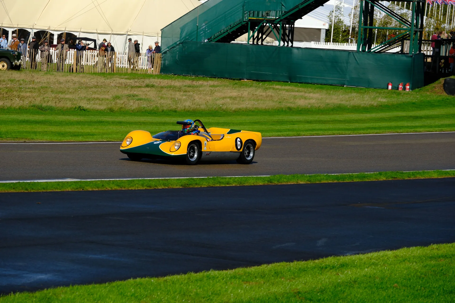 A vibrant yellow vintage racing car speeds around the iconic Goodwood track, capturing classic motorsport essence.