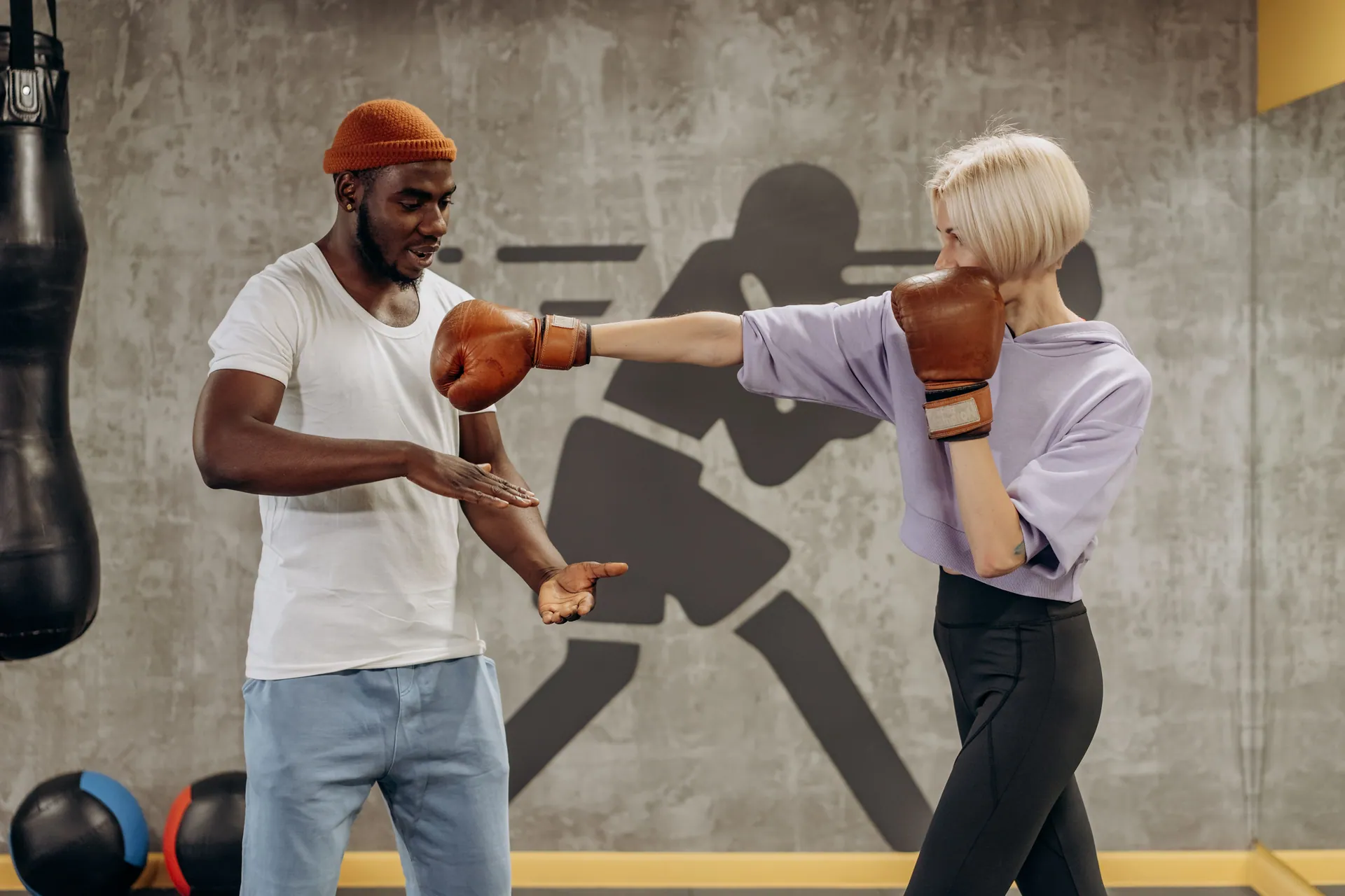 A female boxer in gloves trains with a coach in an indoor gym, focusing on technique.