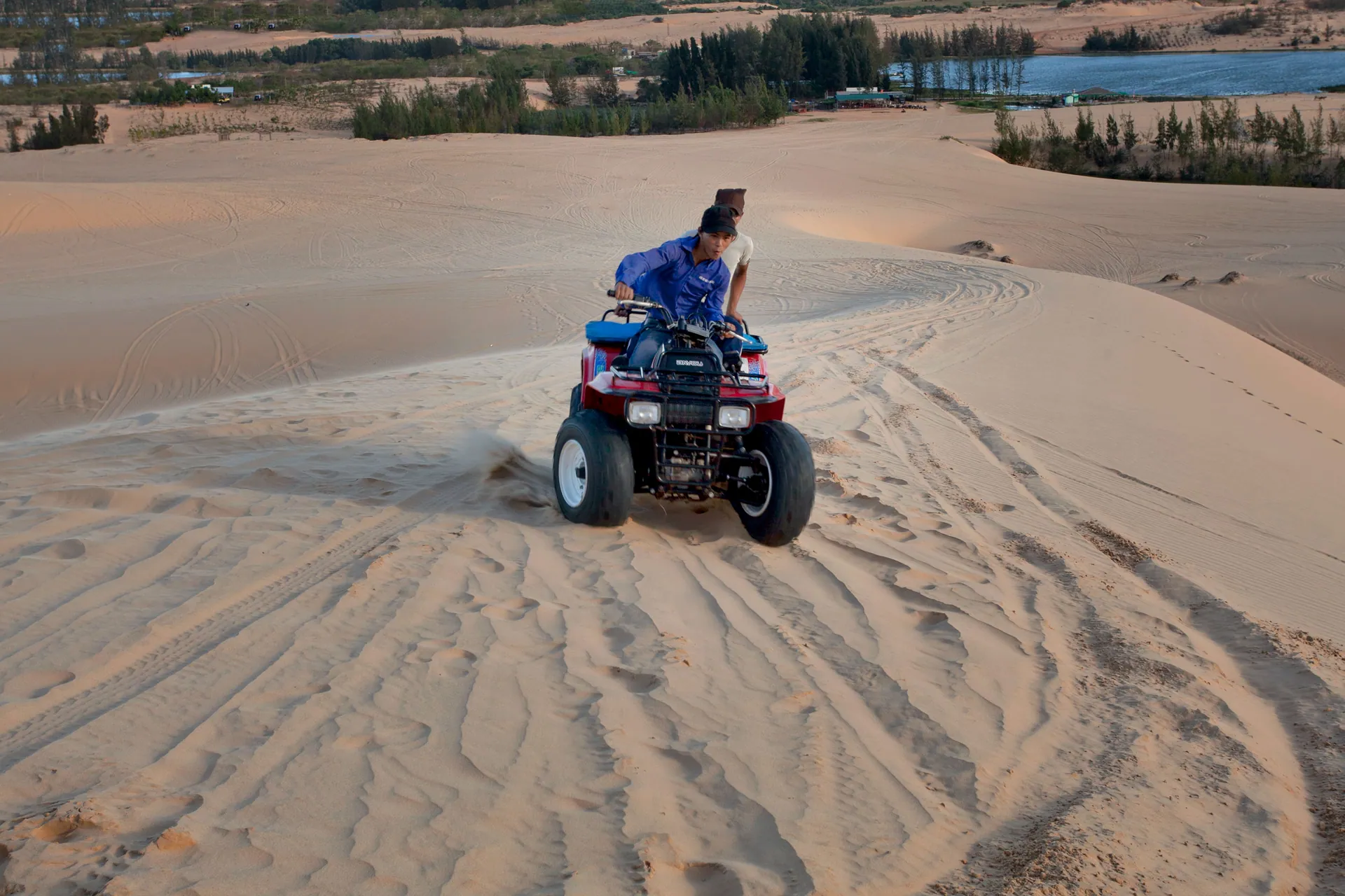 Two people riding an ATV through expansive sand dunes on a sunny day, perfect for adventurous travelers.