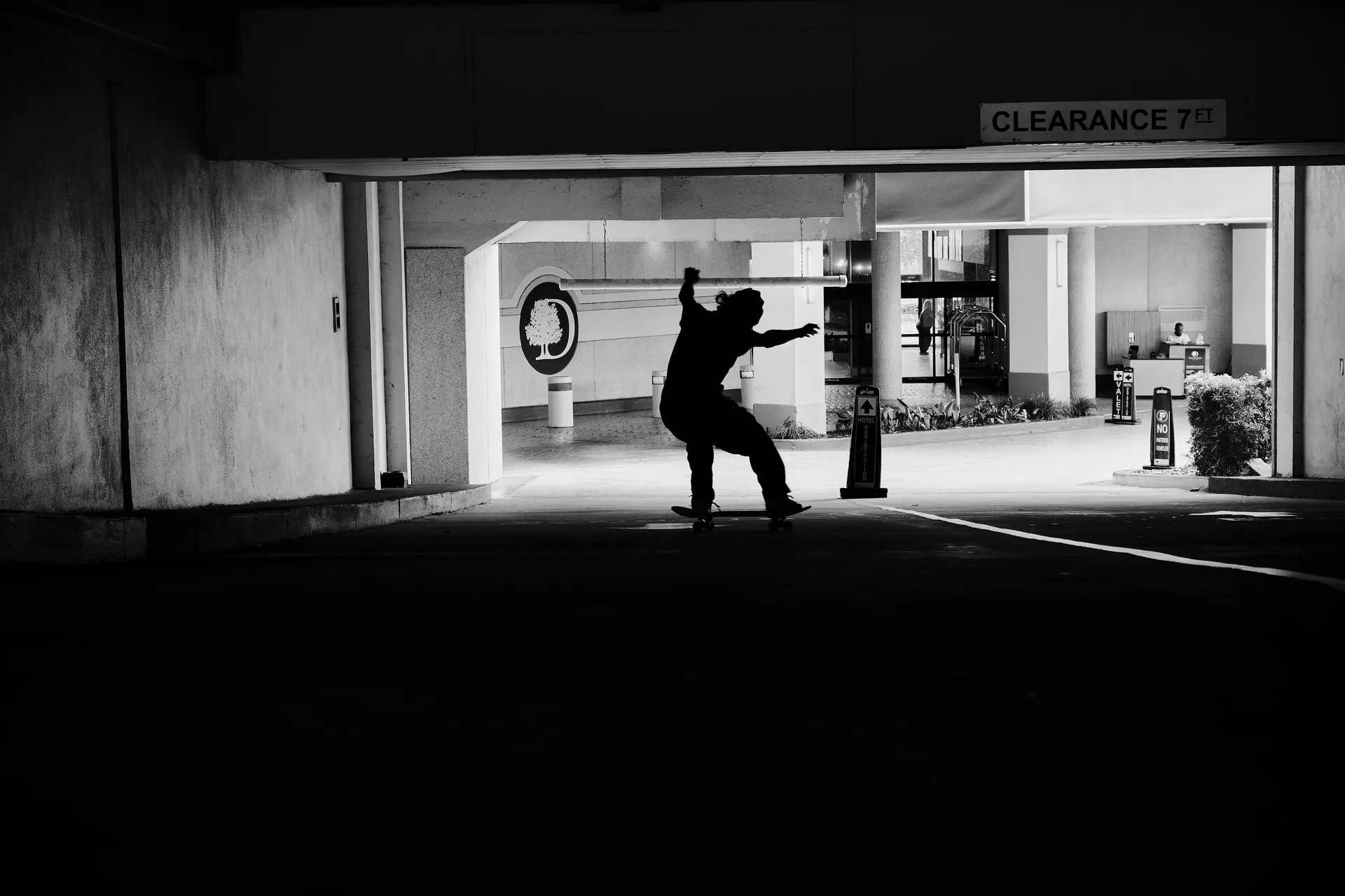 Dynamic black and white silhouette of skateboarder in urban parking structure.