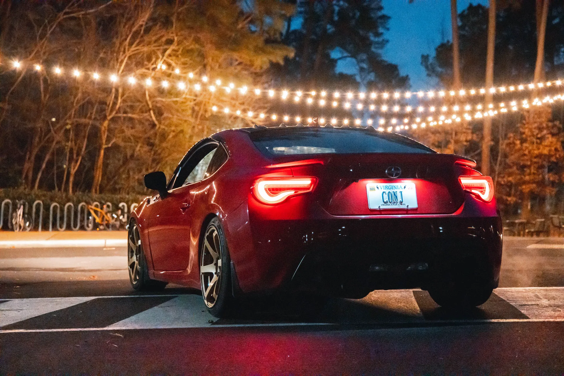 A red sports car under string lights on a festive night road scene.