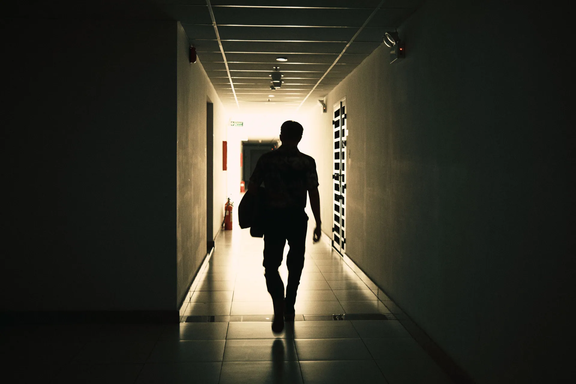 Back view silhouette of unrecognizable male walking on narrow empty hall of modern building