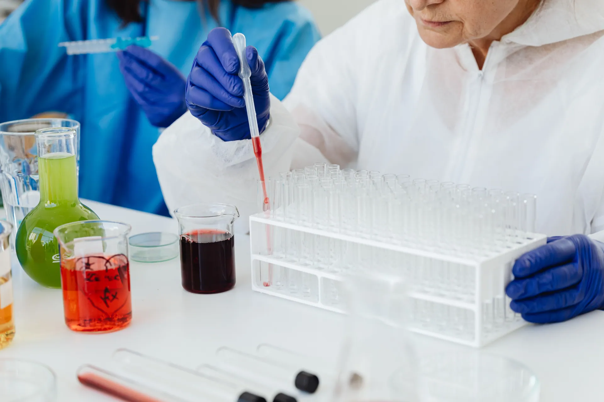 Female scientist in lab coat using pipette on test tubes, focusing on colorful chemical analysis.