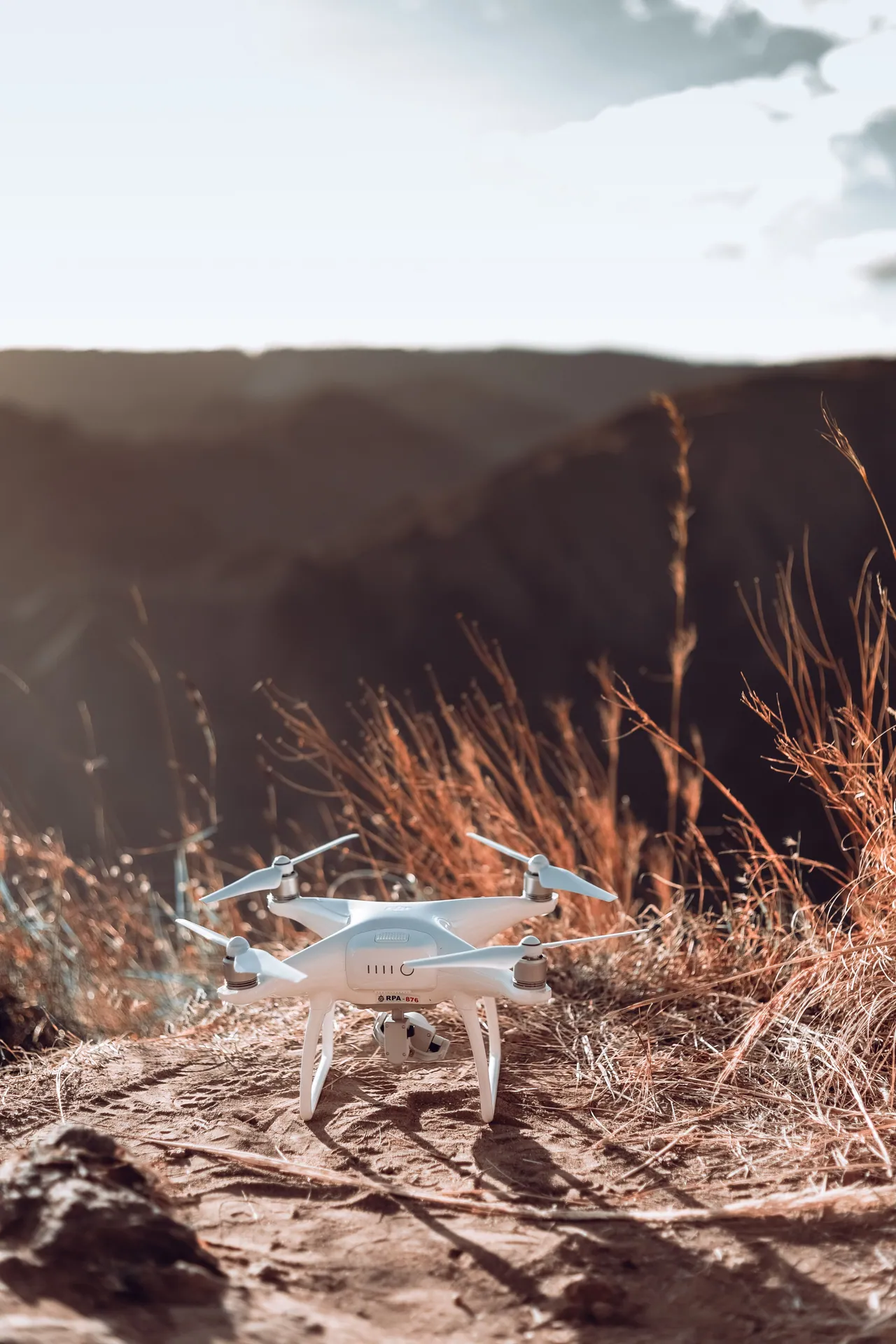 Aerial drone resting on a scenic mountain trail with sunlit grass and distant peaks.