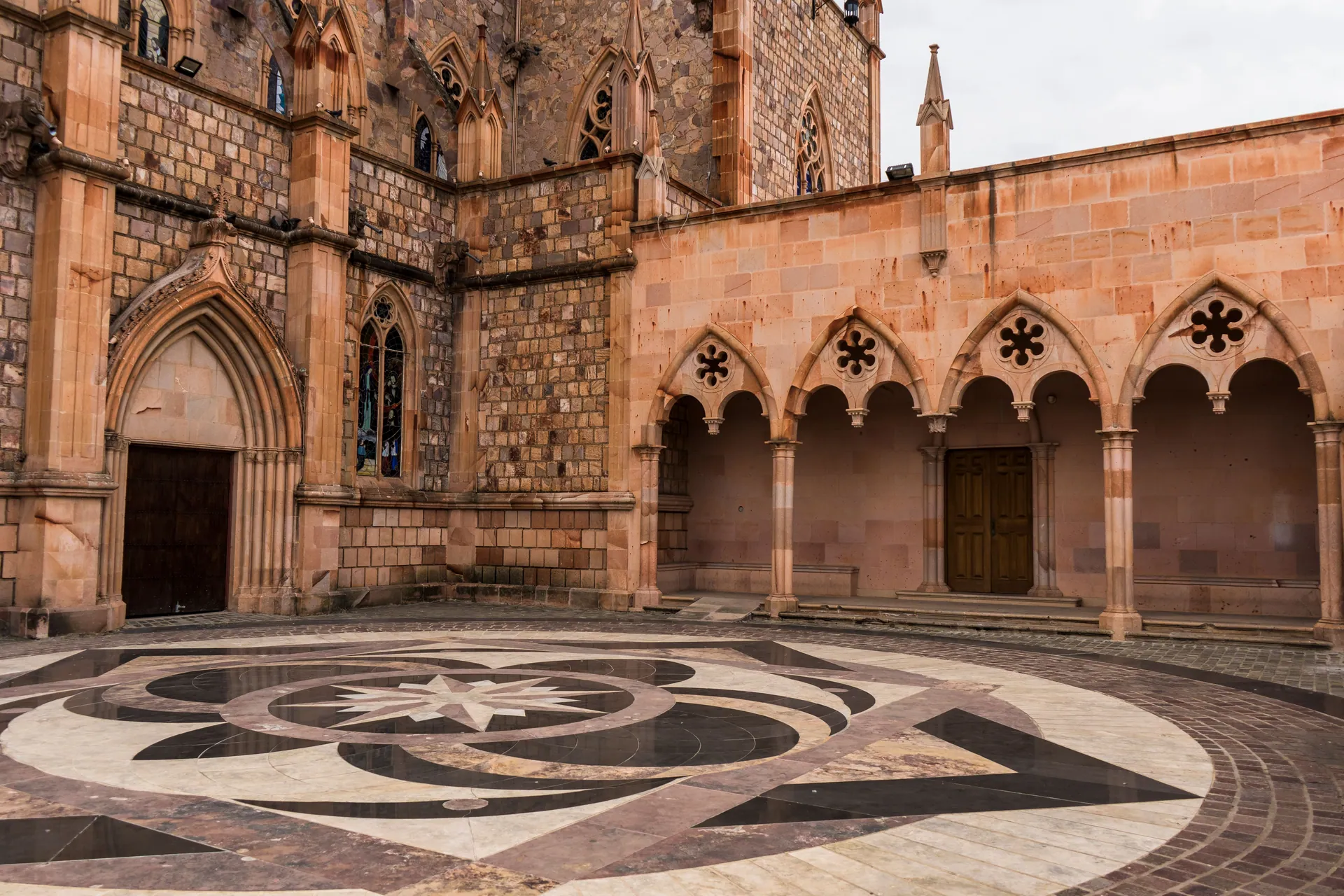 Gothic-style church courtyard featuring stone arches and intricate floor pattern.