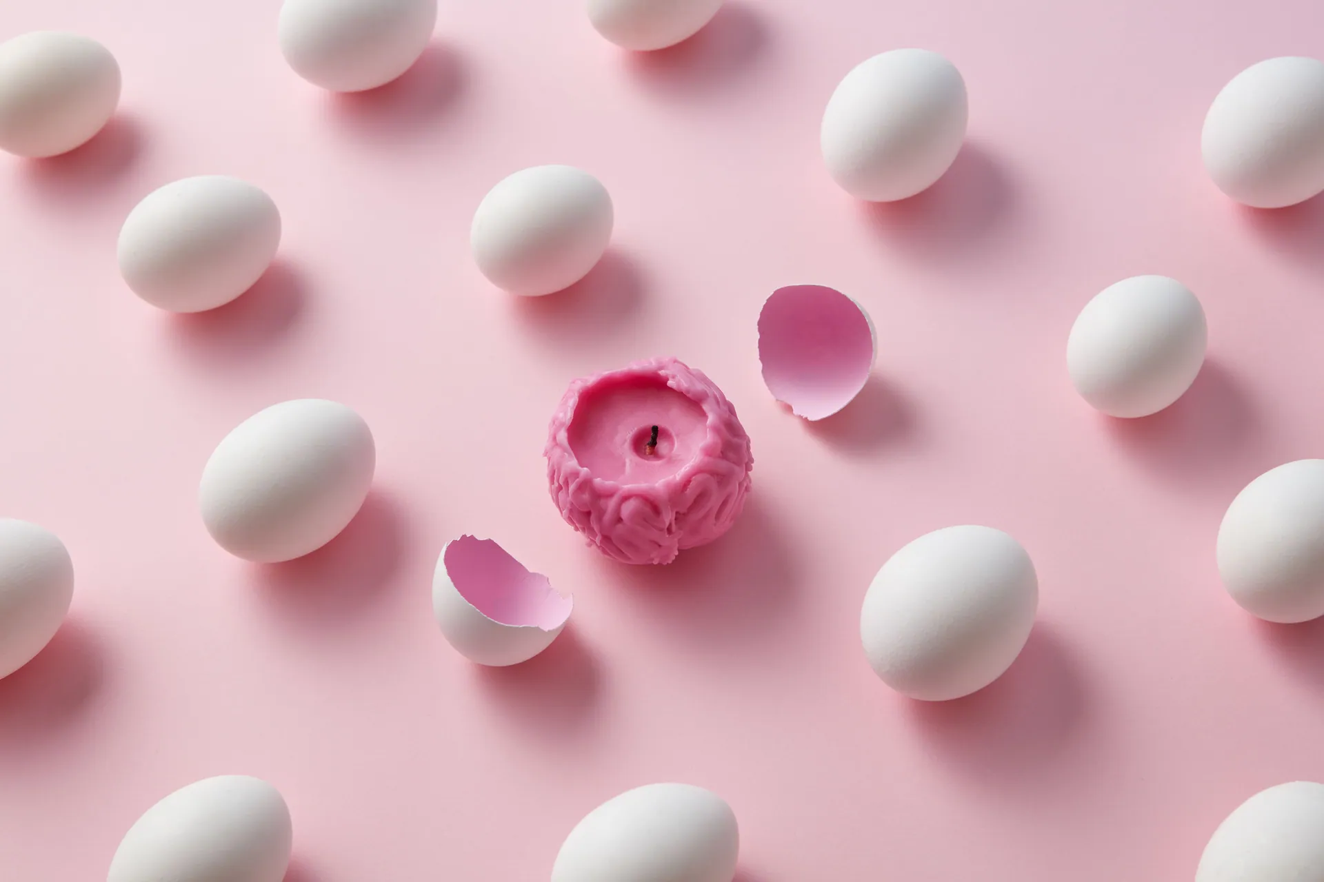 A unique pink brain-shaped candle surrounded by white eggs on a light pink backdrop, depicting creativity and contrast.