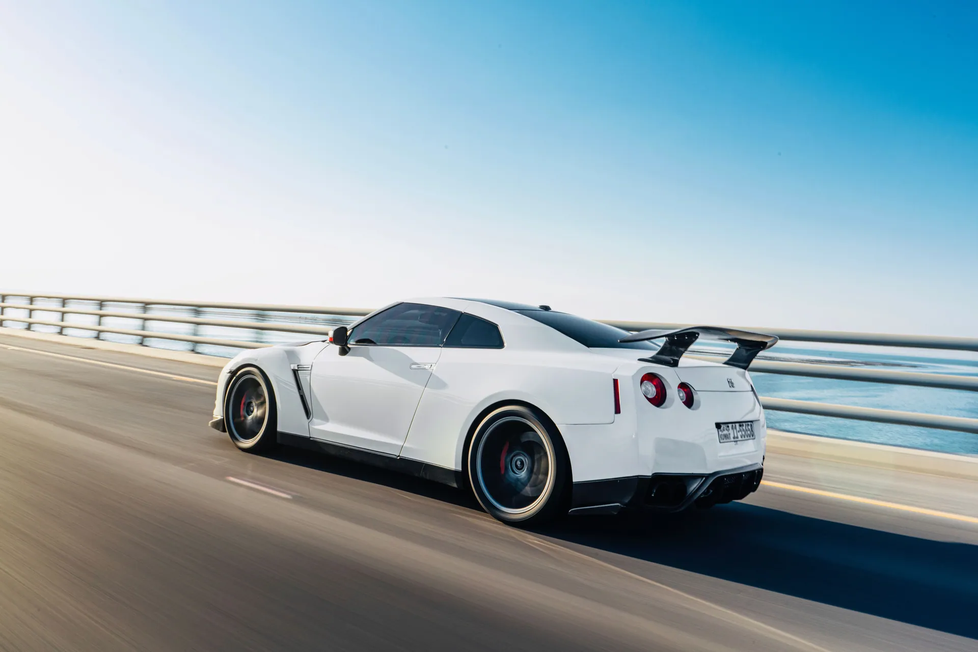 A luxurious white sports car speeding on a scenic coastal highway under clear blue skies.