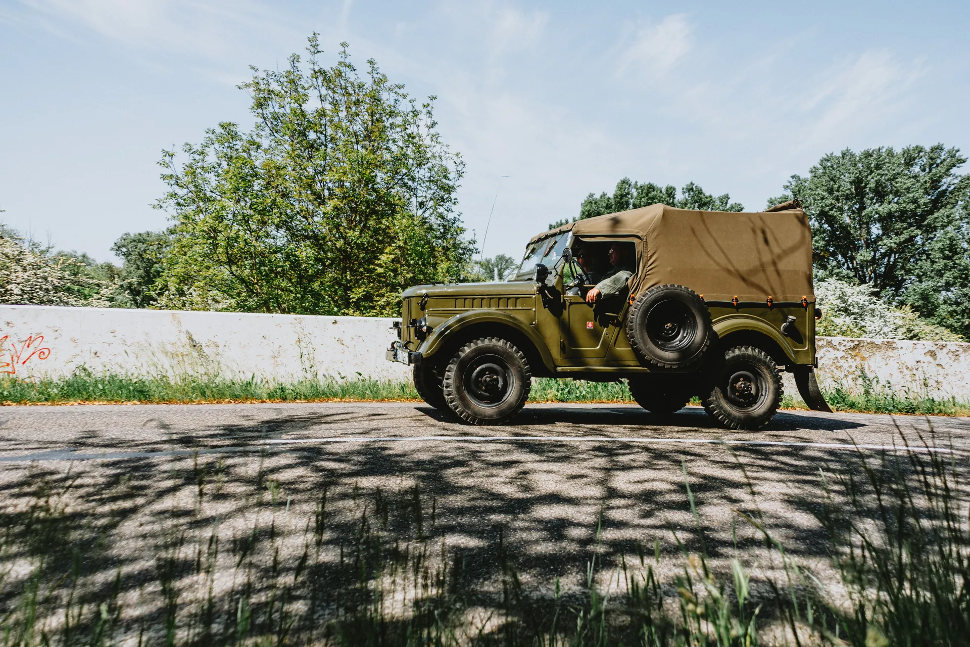 Classic military jeep on a road with clear skies and natural surroundings.