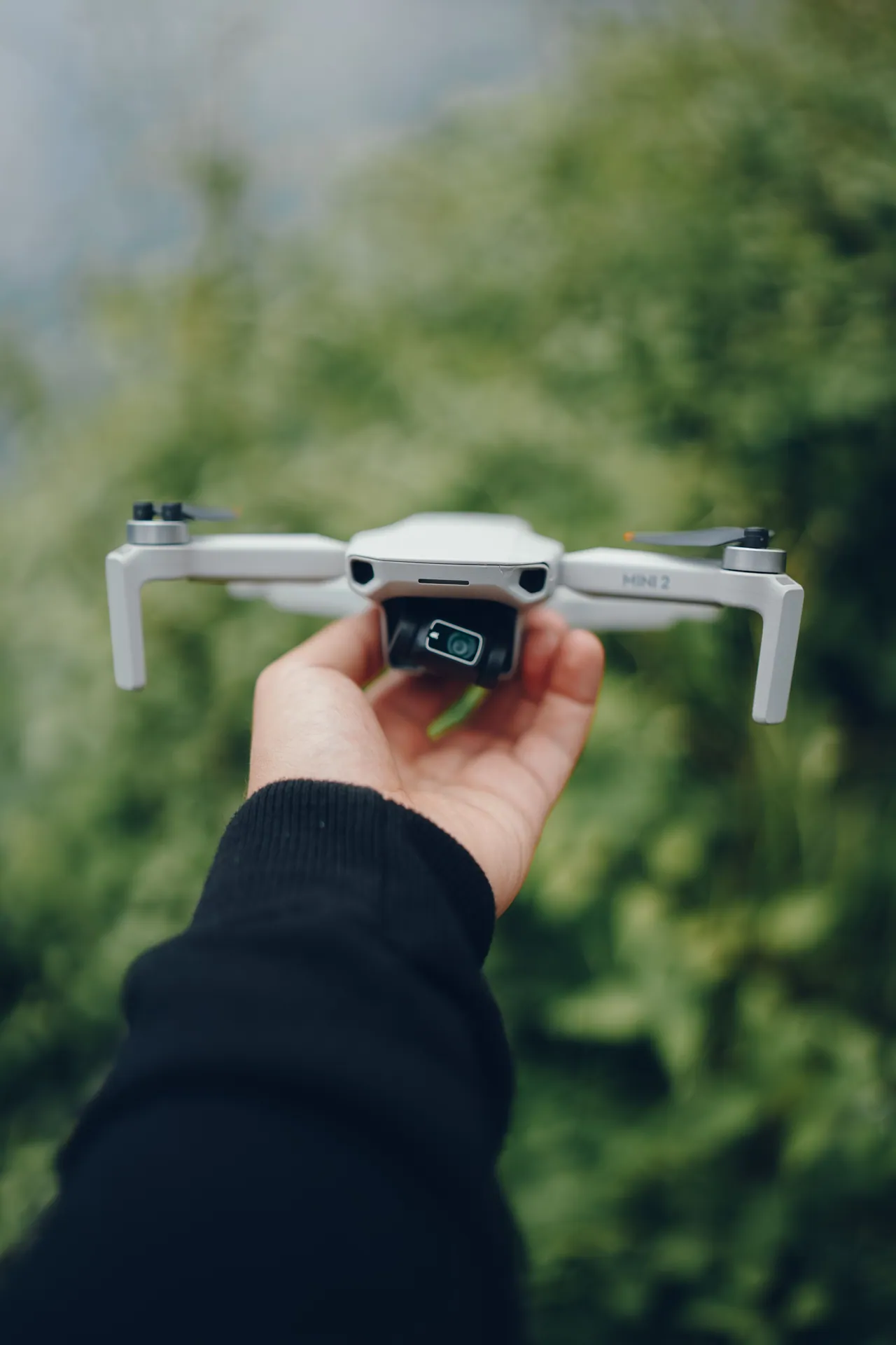 Hand holding a compact drone against a blurred natural background, perfect for tech and outdoor enthusiasts.