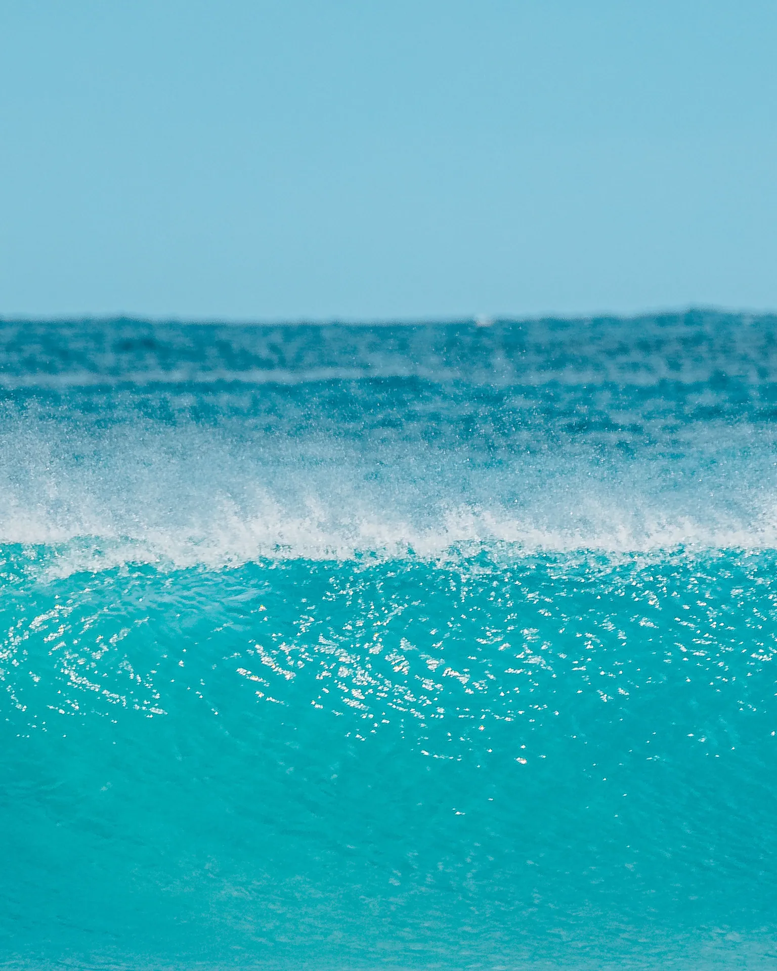 Vibrant ocean wave crashing under a clear blue sky, capturing the serenity of nature.