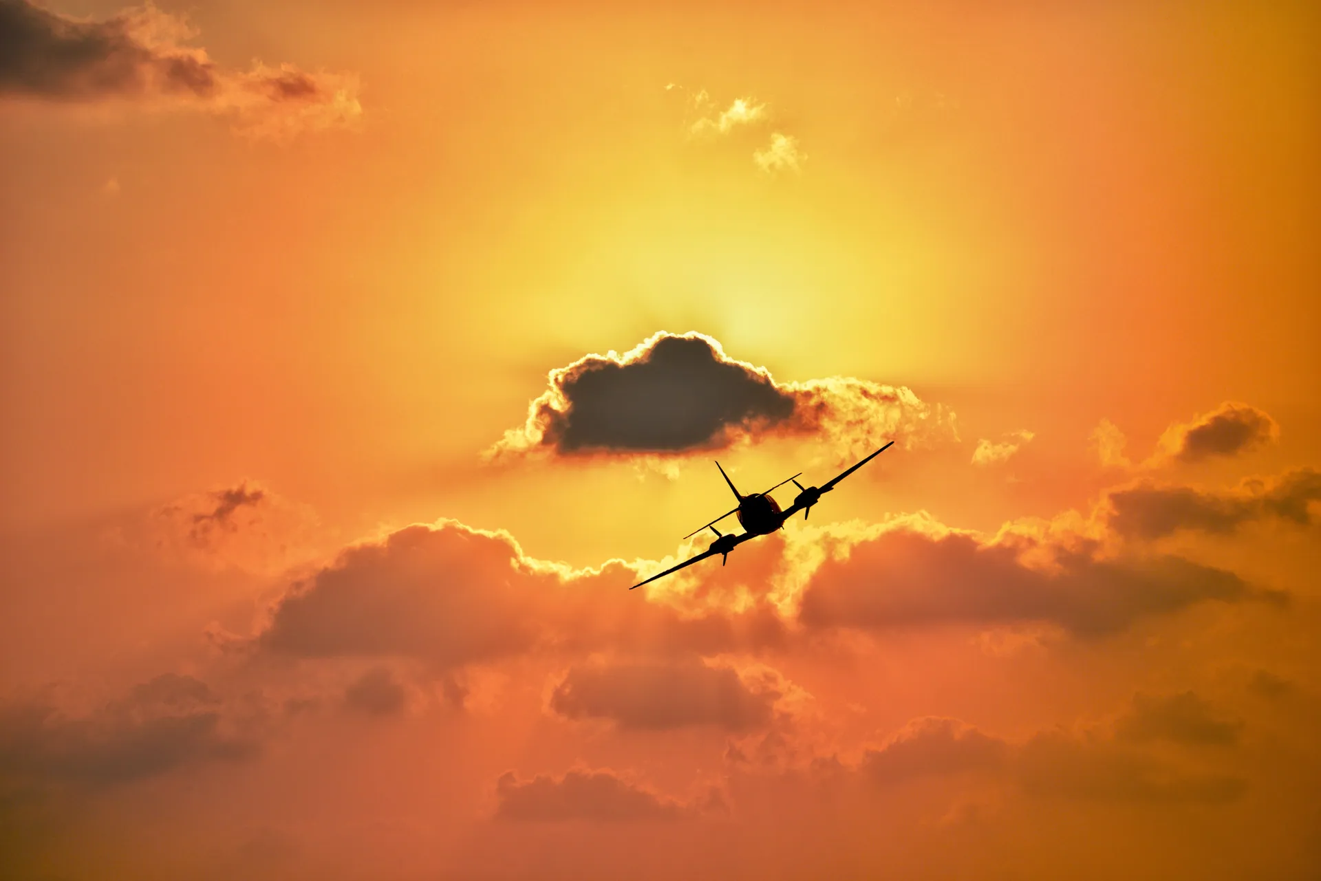 A silhouette of an airplane flying against a vibrant sunset sky with clouds in Kish, Iran.