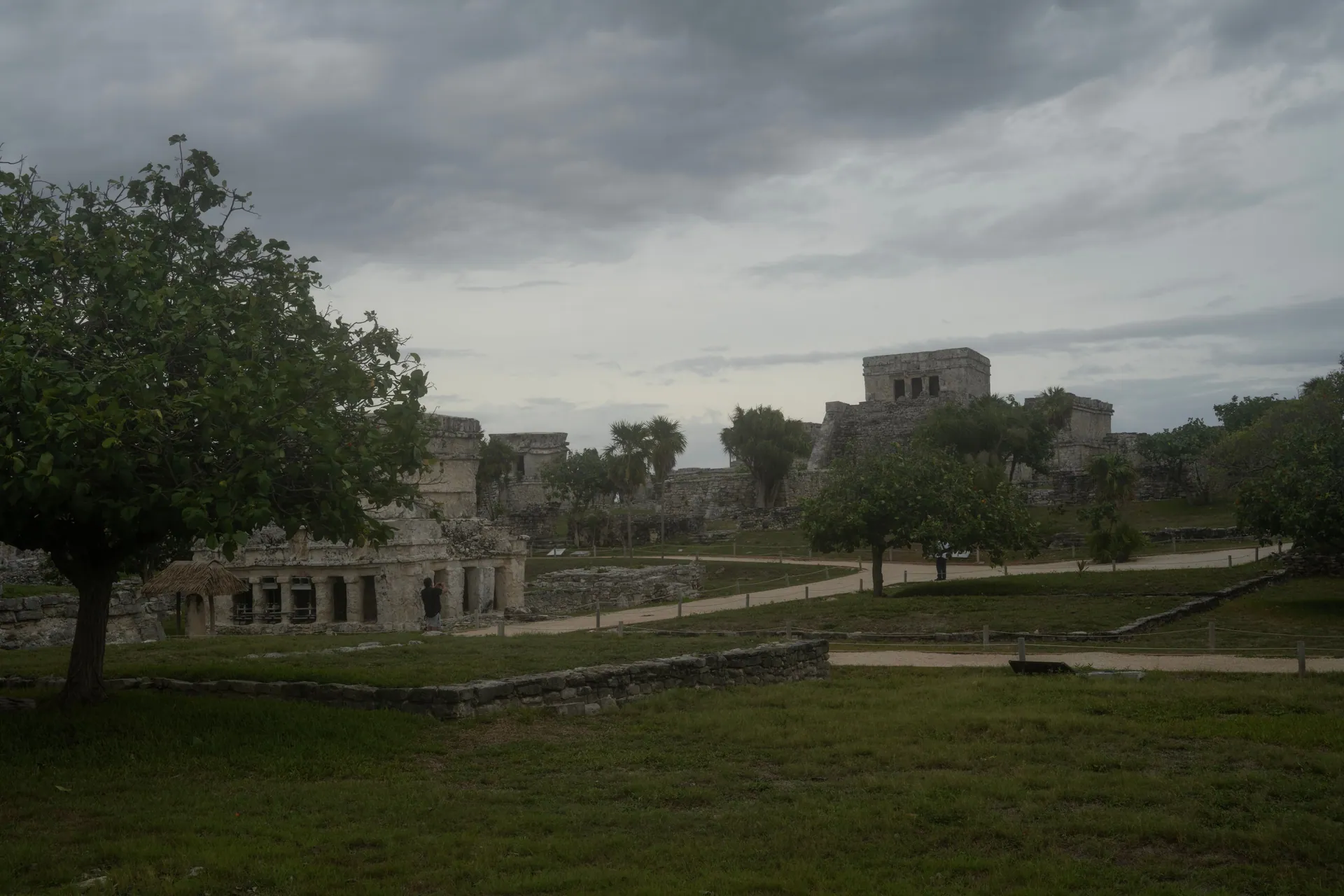 Explore the historic ruins of Tulum in Mexico surrounded by lush trees and overcast skies.