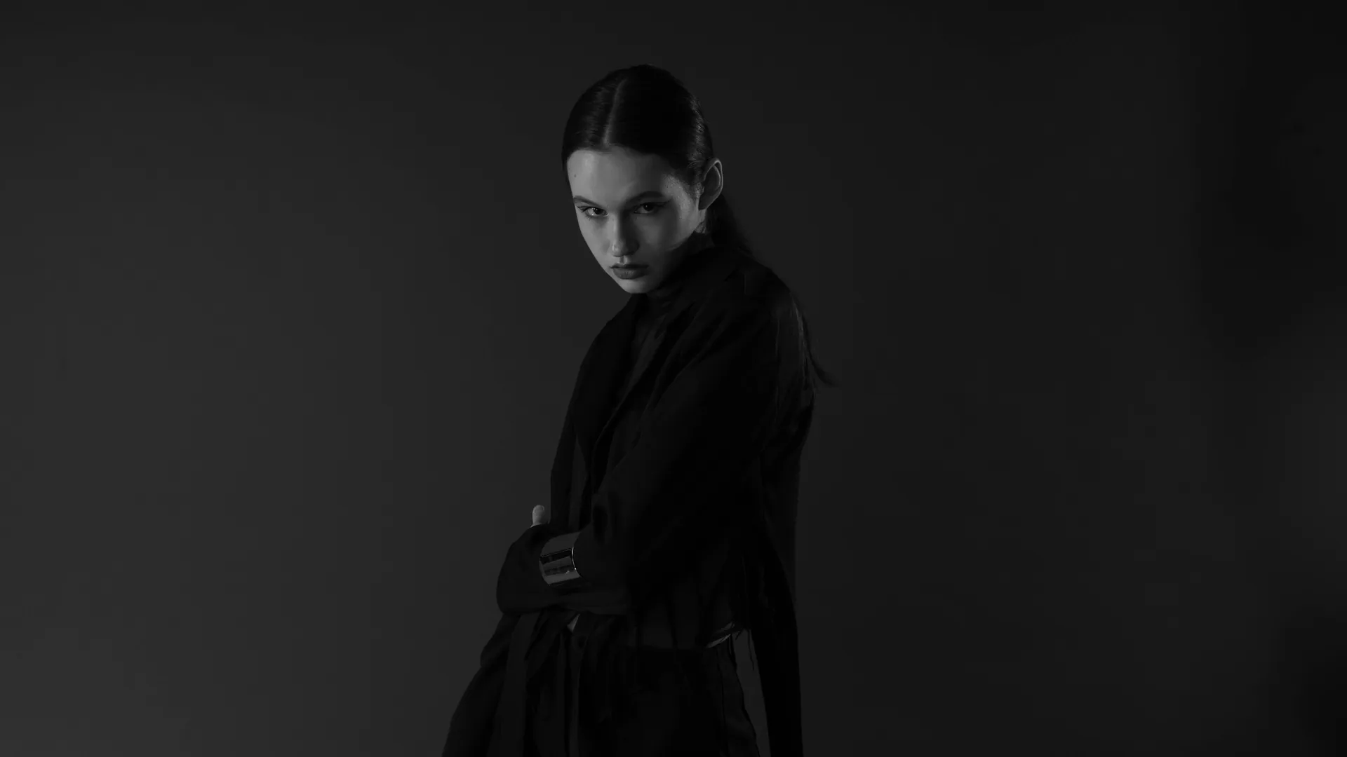 Black and white studio portrait of a woman exuding elegance in a dark coat.