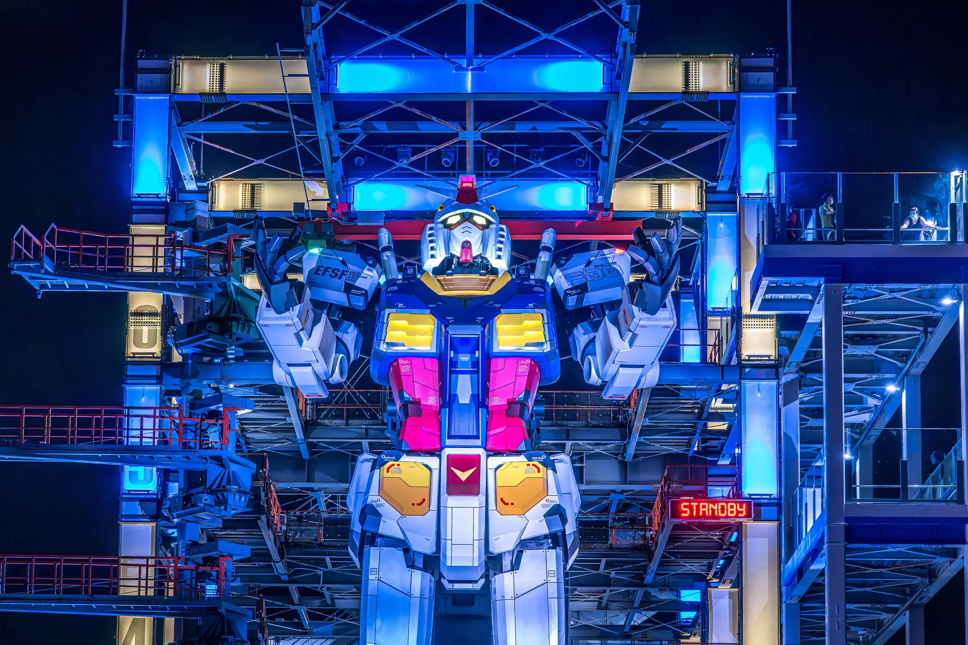 Illuminated Gundam robot at Yokohama's Gundam Factory lit up at night. Vibrant colors and futuristic design.