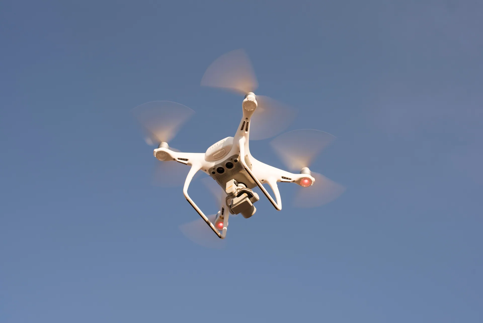 A white drone in flight against a clear blue sky, capturing aerial footage with precision.