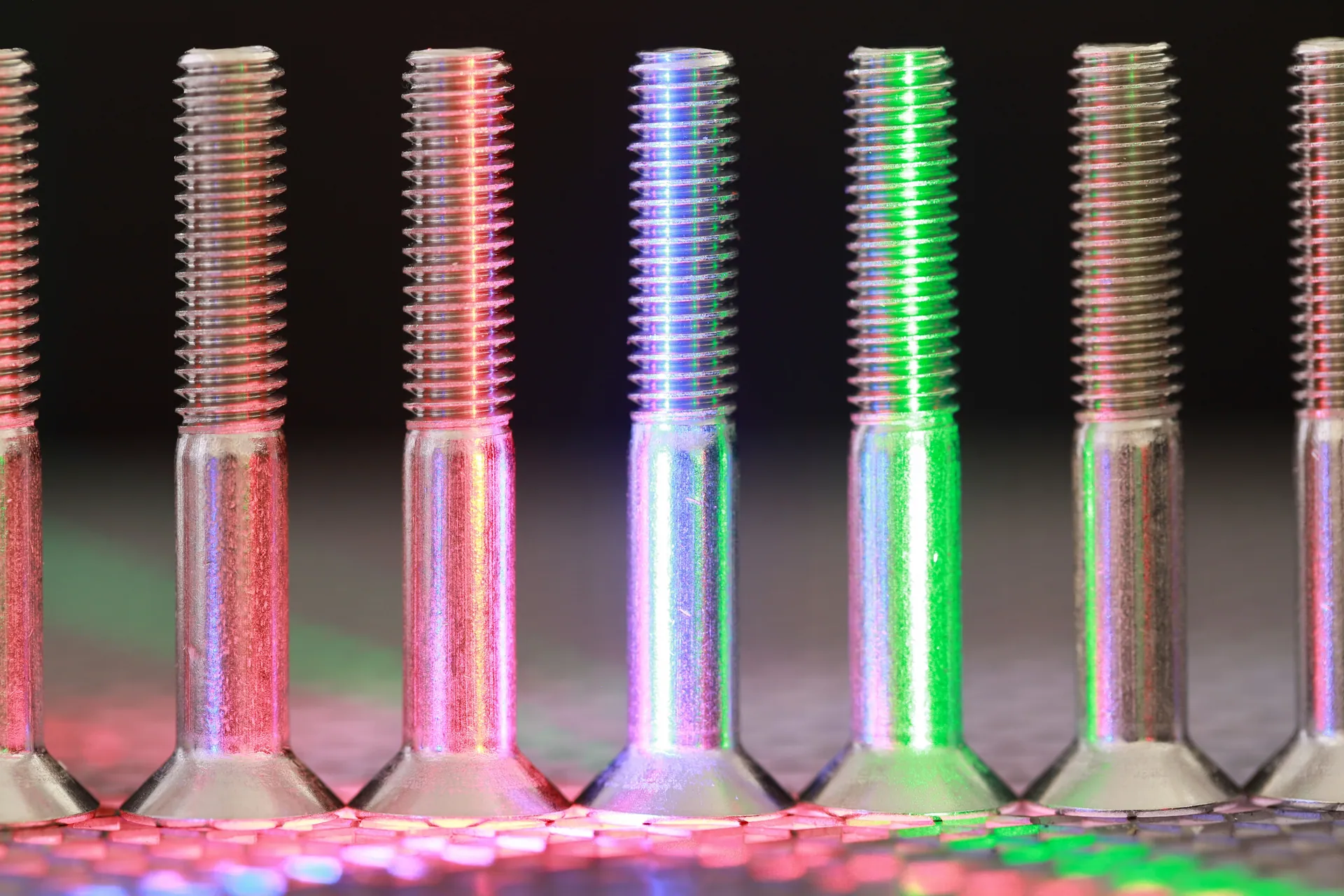 Vibrant close-up of metallic bolts featuring multicolored neon lighting effect.