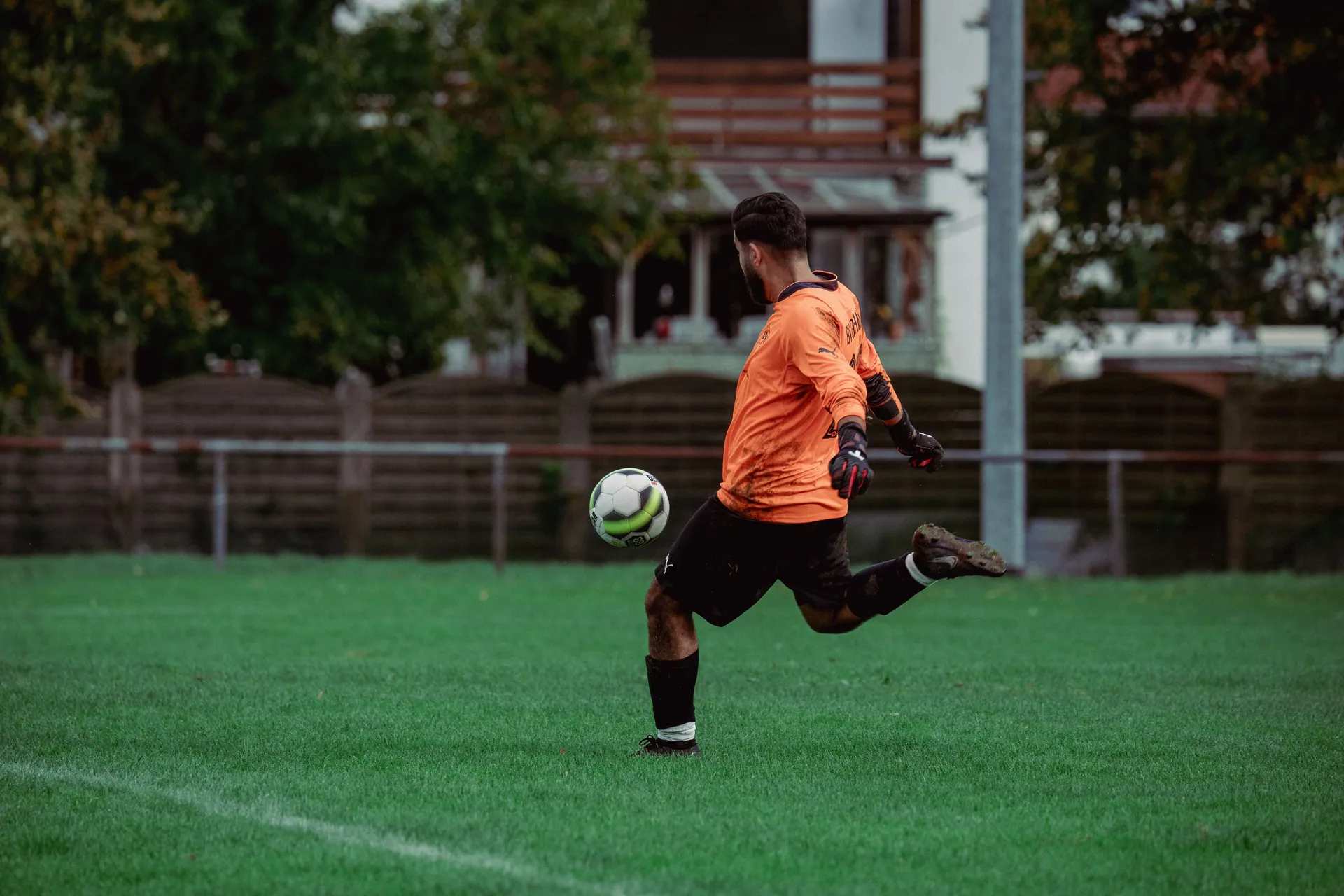 Soccer player in orange jersey kicking a ball on a lush green field during a daytime game.