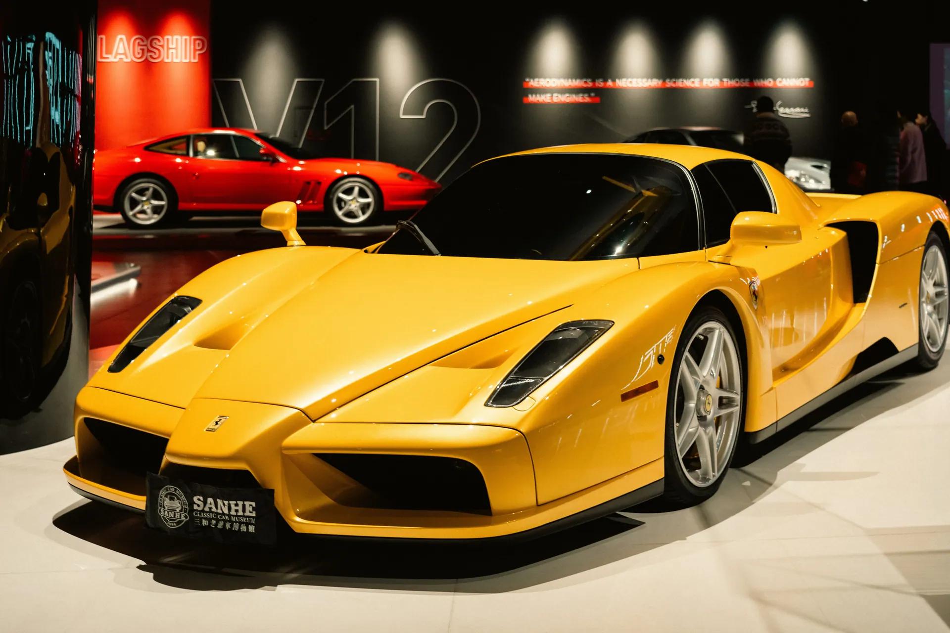 Yellow luxury sports car with a red car in the background at an auto exhibition.