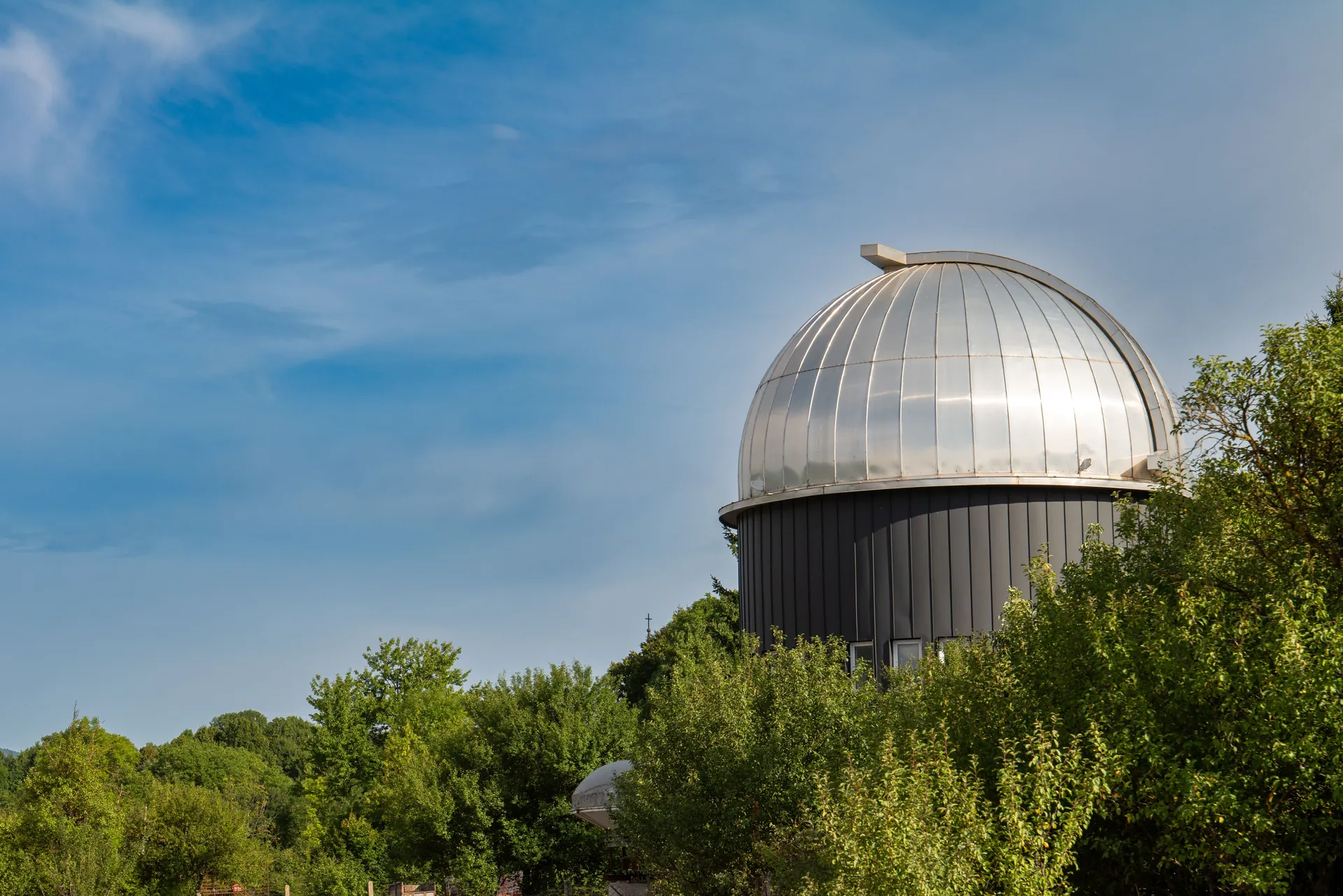 A large observatory dome surrounded by lush trees under a clear blue sky in Korenica, Croatia.