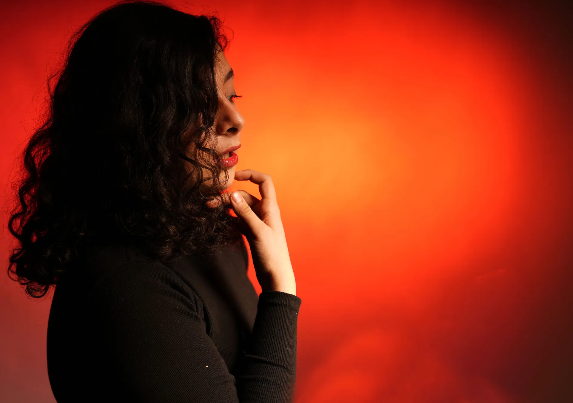 Profile of a woman with curly hair pondering, set against a vivid red backdrop.