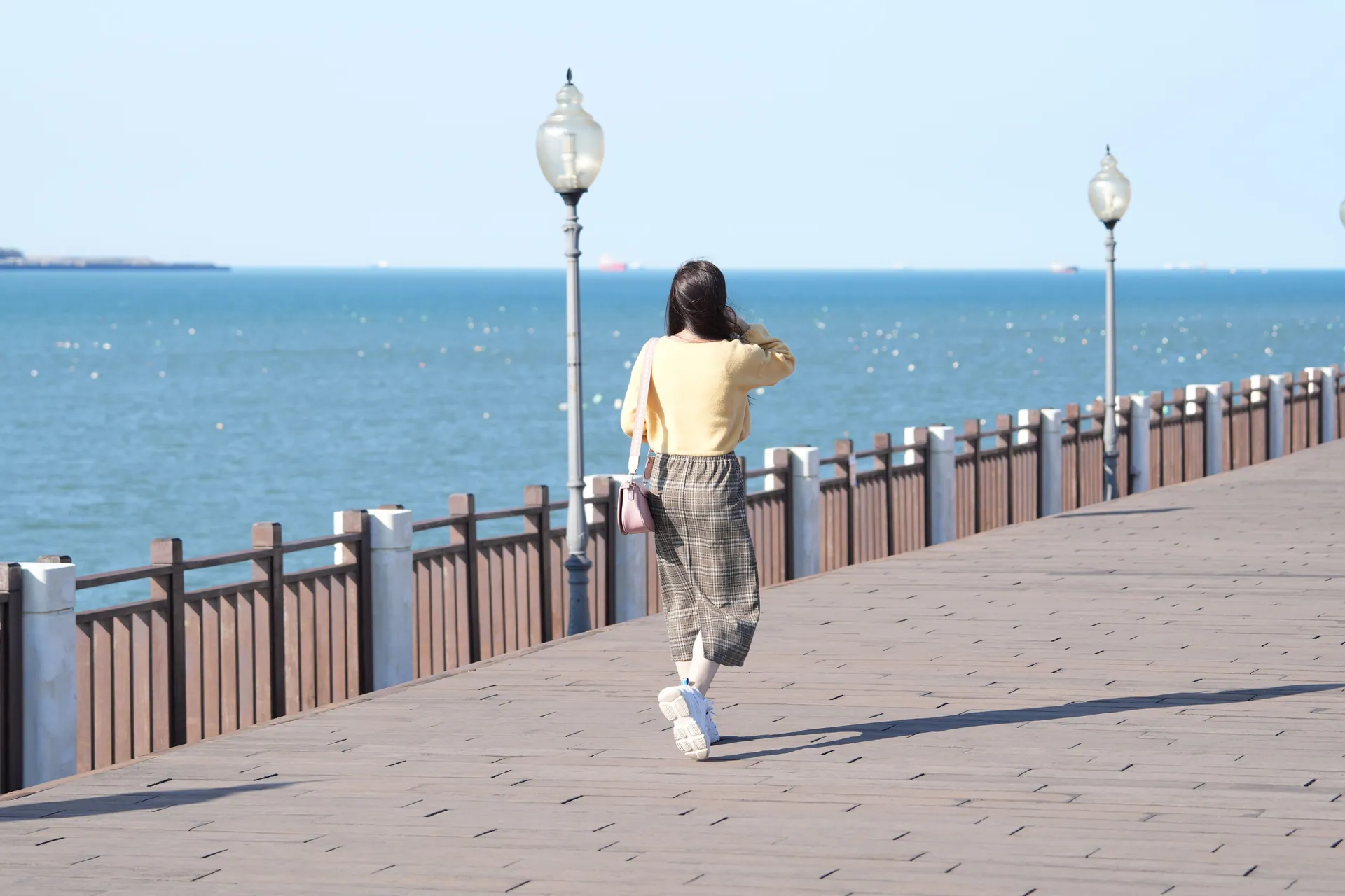 A woman walks on a pier by the ocean, enjoying the sunny day.