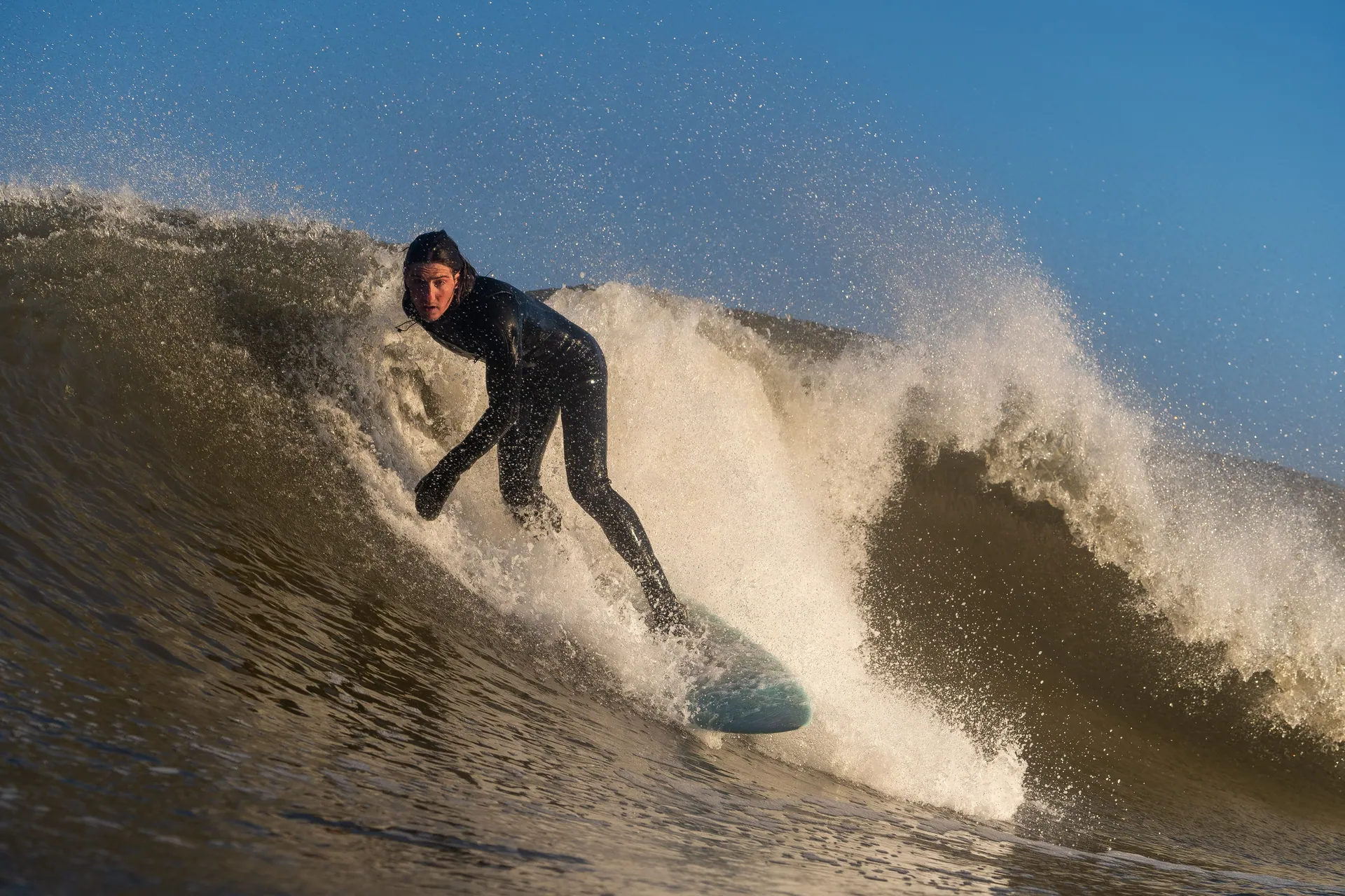 Dynamic image of a surfer riding a powerful ocean wave in a wetsuit during the day.