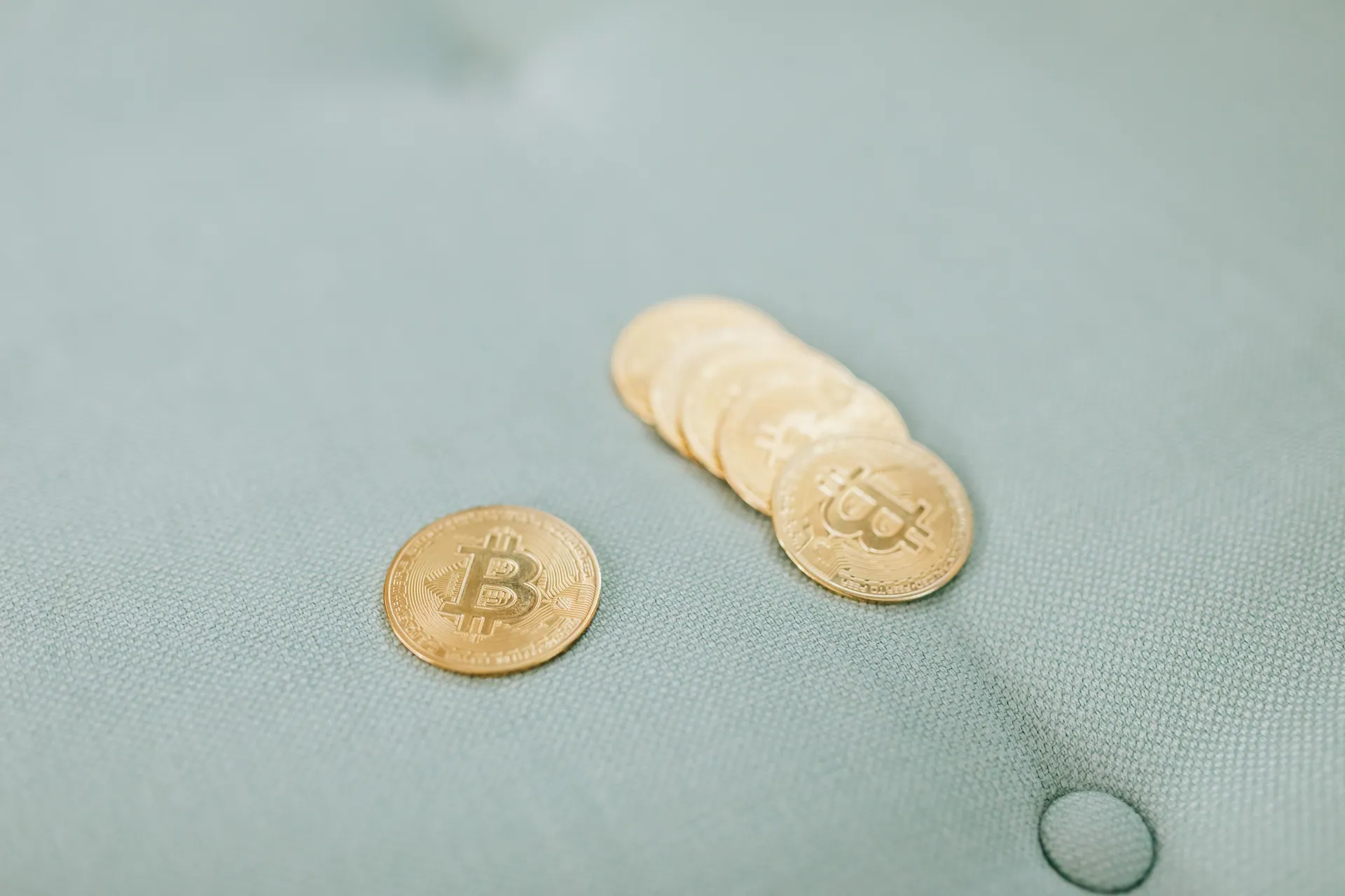 Close-up of gold Bitcoins laid on a soft blue fabric background, representing cryptocurrency wealth.