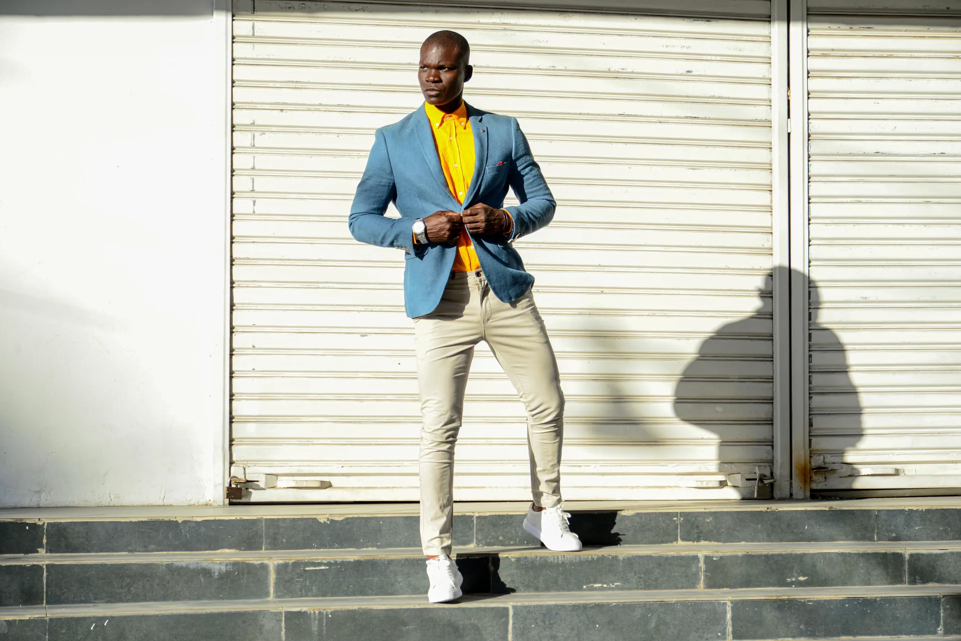 Elegant man in a colorful outfit poses stylishly against a roller shutter outdoors.
