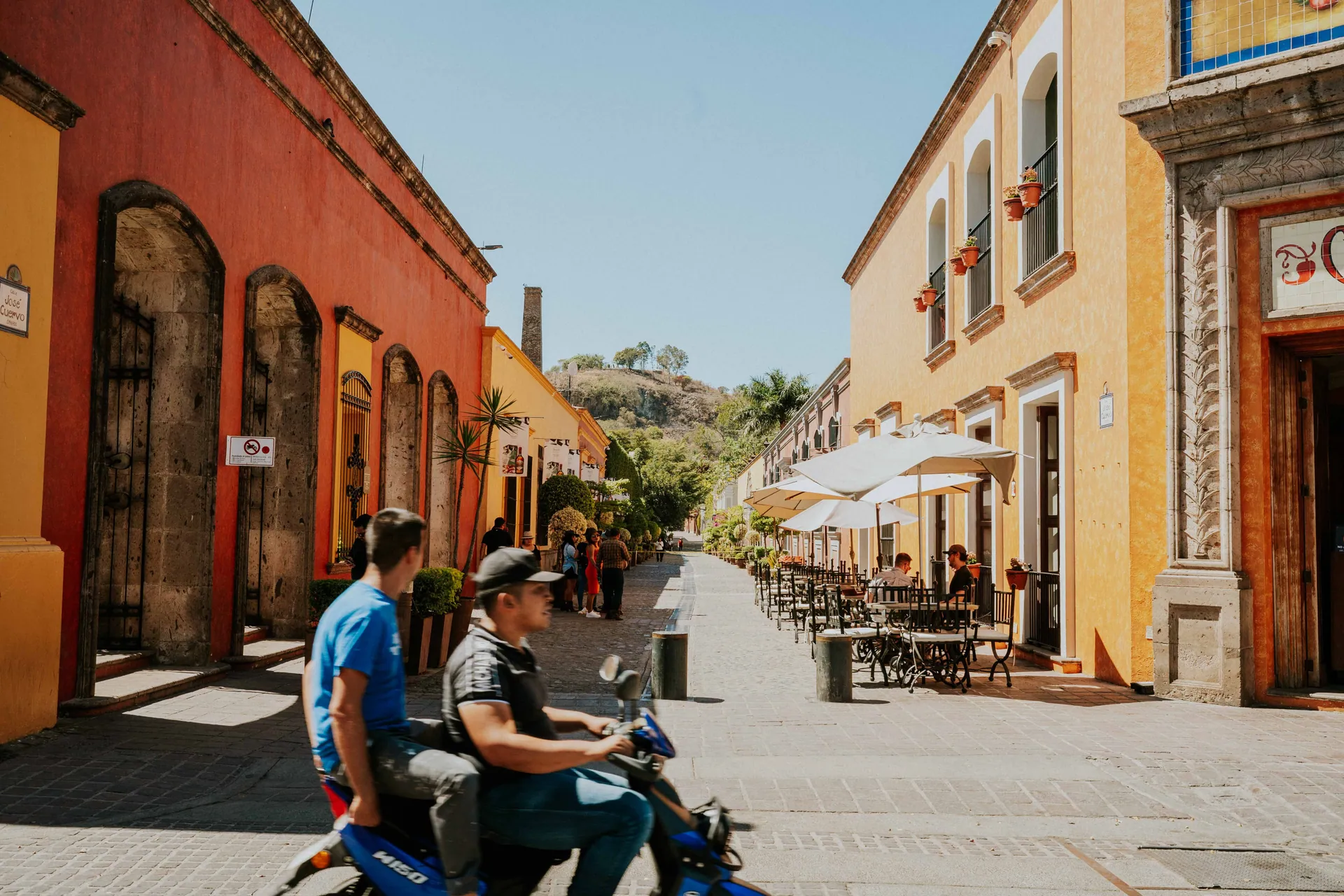 Vibrant street in Tequila, Jalisco with people enjoying a sunny day and colorful architecture.