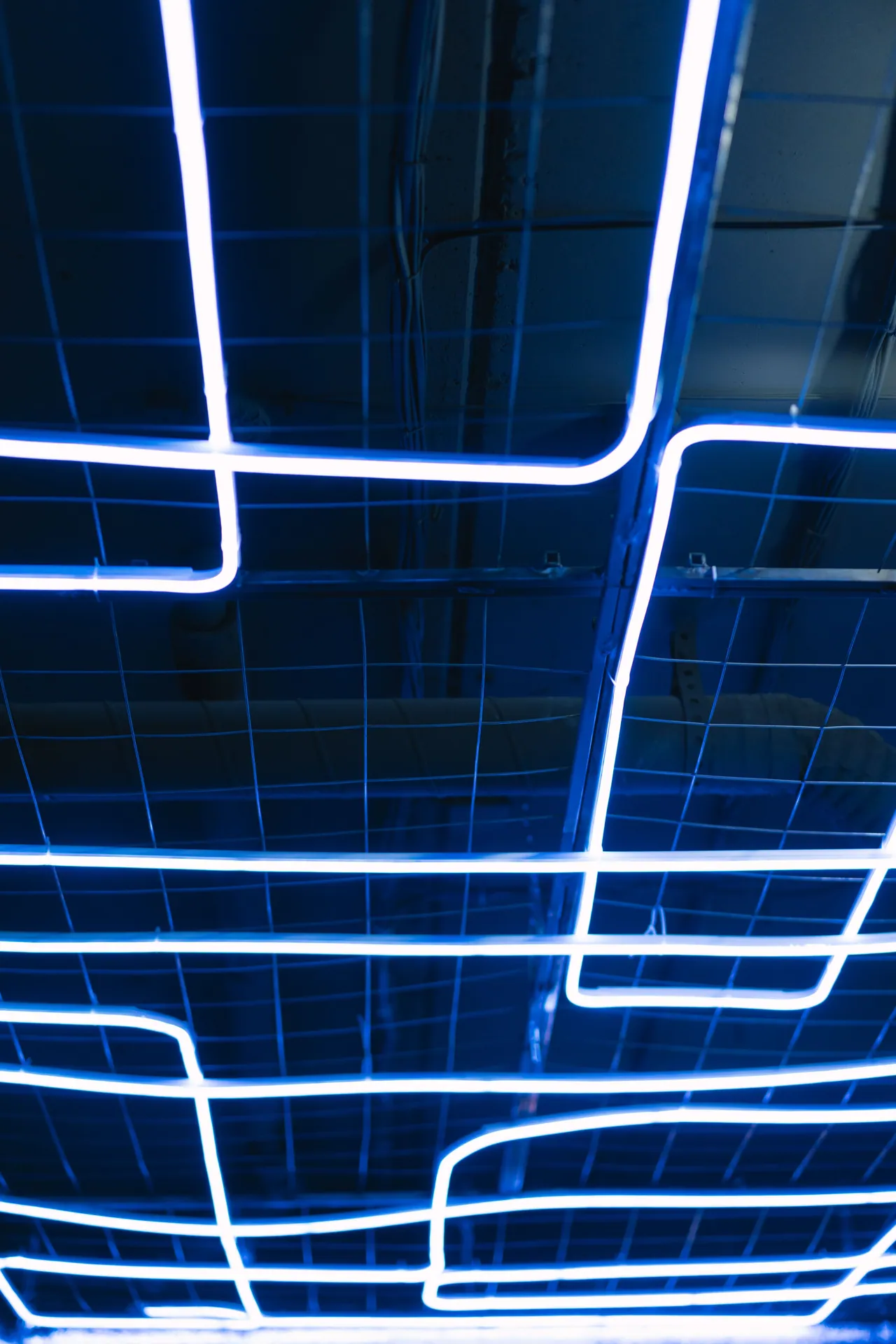 Abstract blue neon light art installation with geometric patterns on a grid.