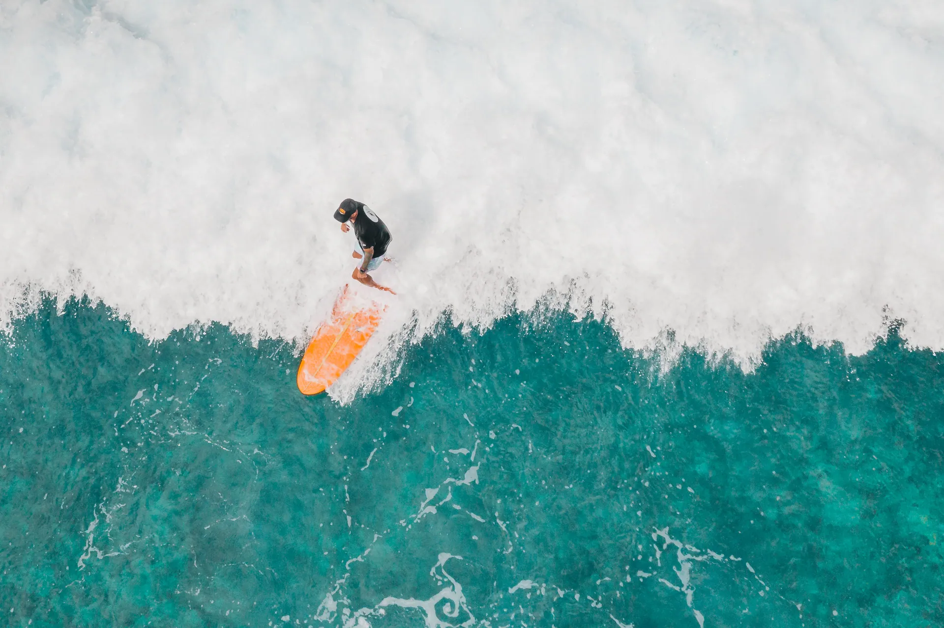 Aerial view of a surfer with an orange surfboard riding a wave in the ocean.