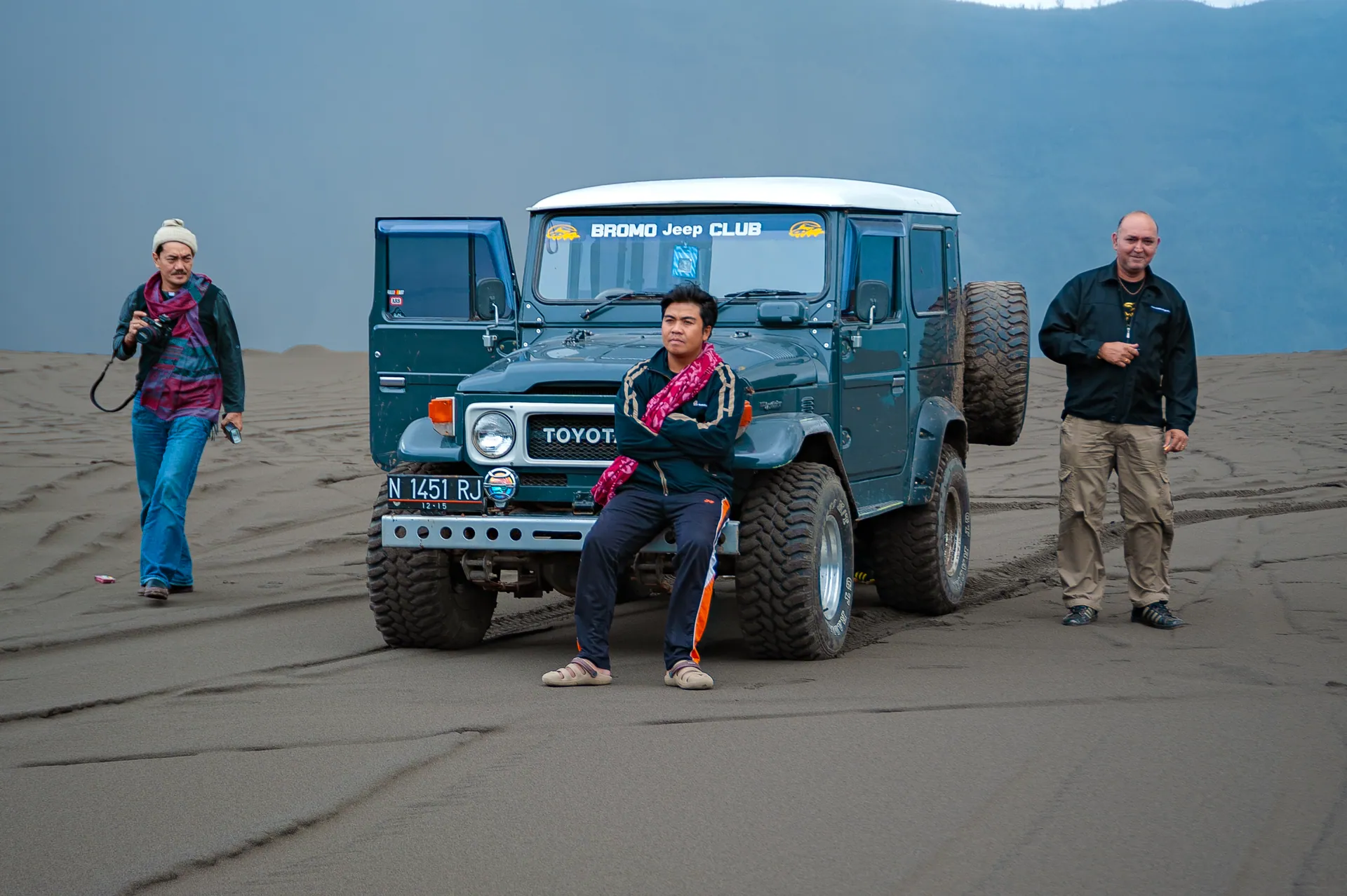 Three adults with a jeep explore a desert landscape, showcasing travel and adventure.