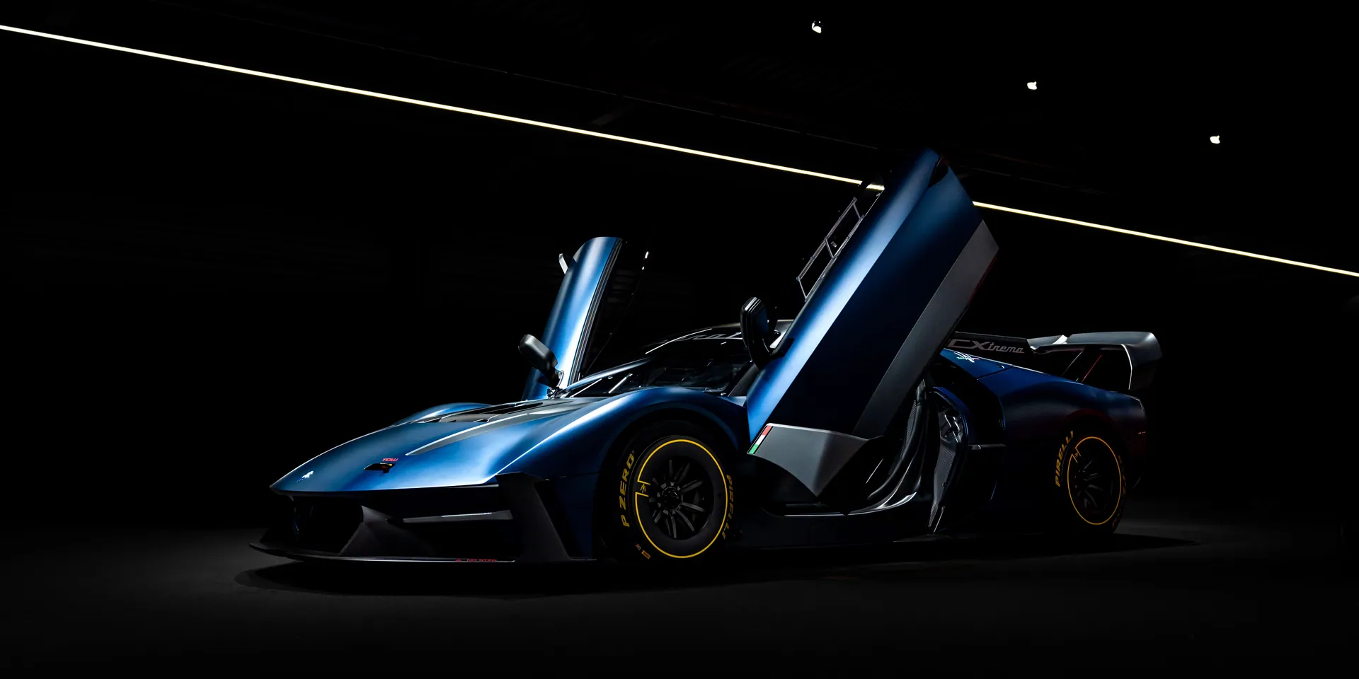 Sleek blue sports car with open vertical doors in a dark setting.