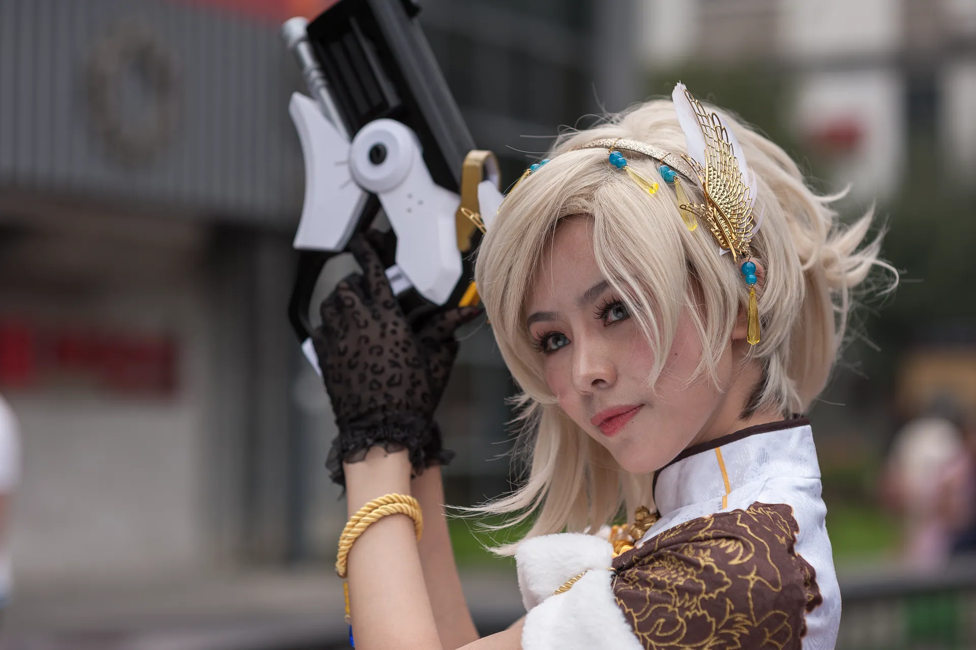 Cosplayer with intricate costume and prop gun, posing outdoors during the day.
