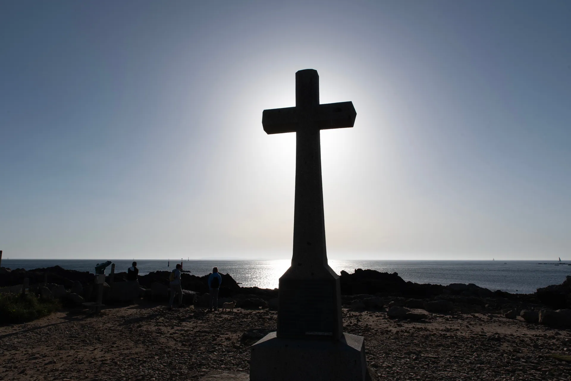 Dramatic silhouette of a cross with people by the ocean at sunset, conveying peace and reflection.