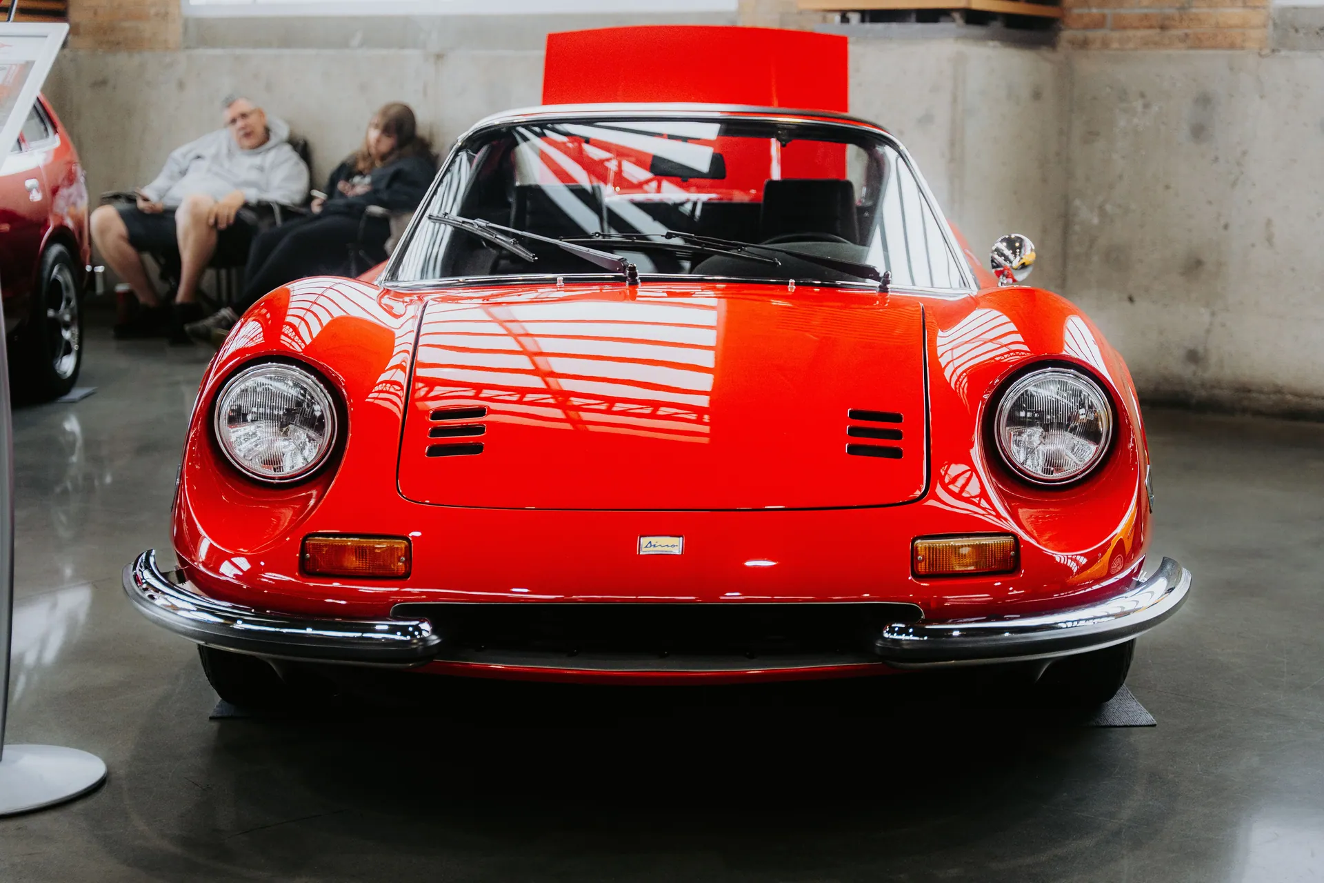 Front view of a classic red sports car displayed indoors at an auto show.