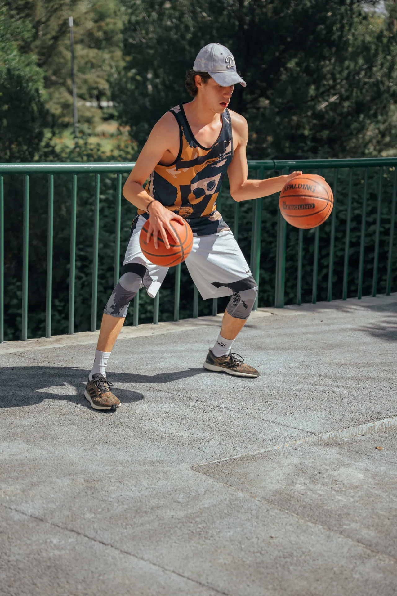 Young man practicing basketball dribbling with two balls outdoors in sportswear.