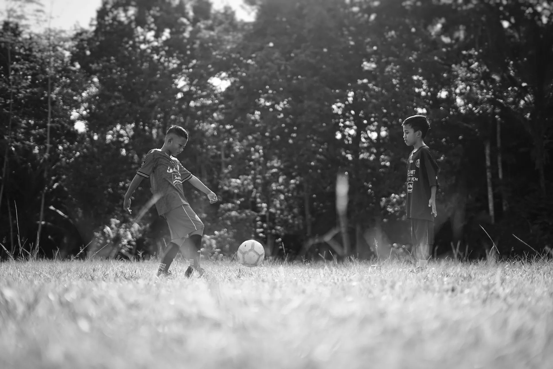 Two young boys playing soccer on a sunny day in a park, enjoying the outdoors.