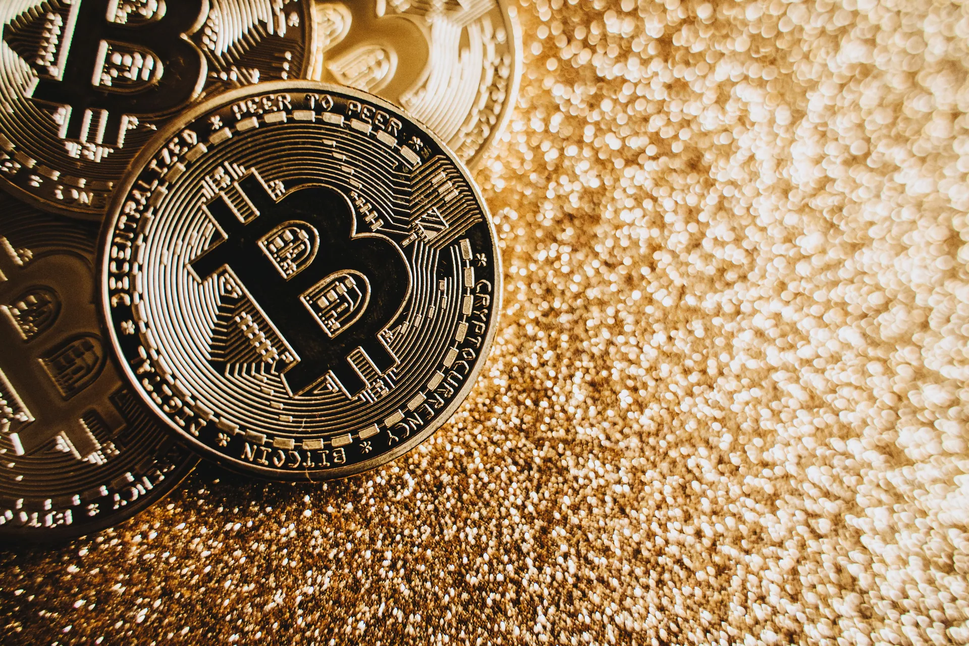 Close-up view of shining Bitcoin coins on a glittering golden background representing digital wealth.