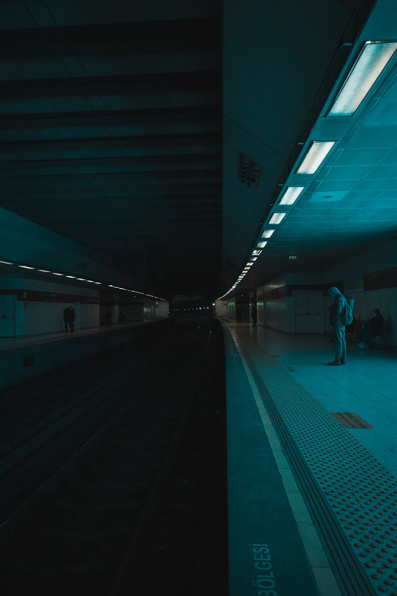 A quiet, dimly lit subway platform with a solitary commuter captured in a moody atmosphere.