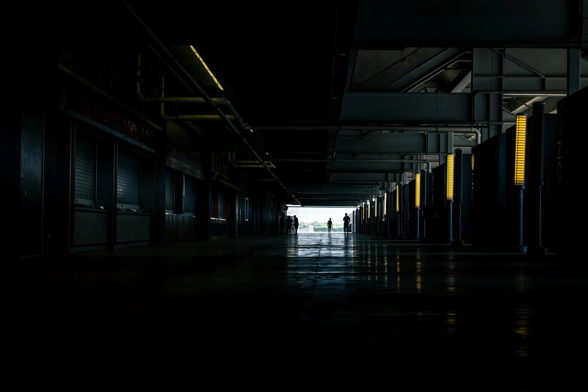 A long, dark industrial corridor with silhouetted figures in the distance, creating a moody atmosphere.